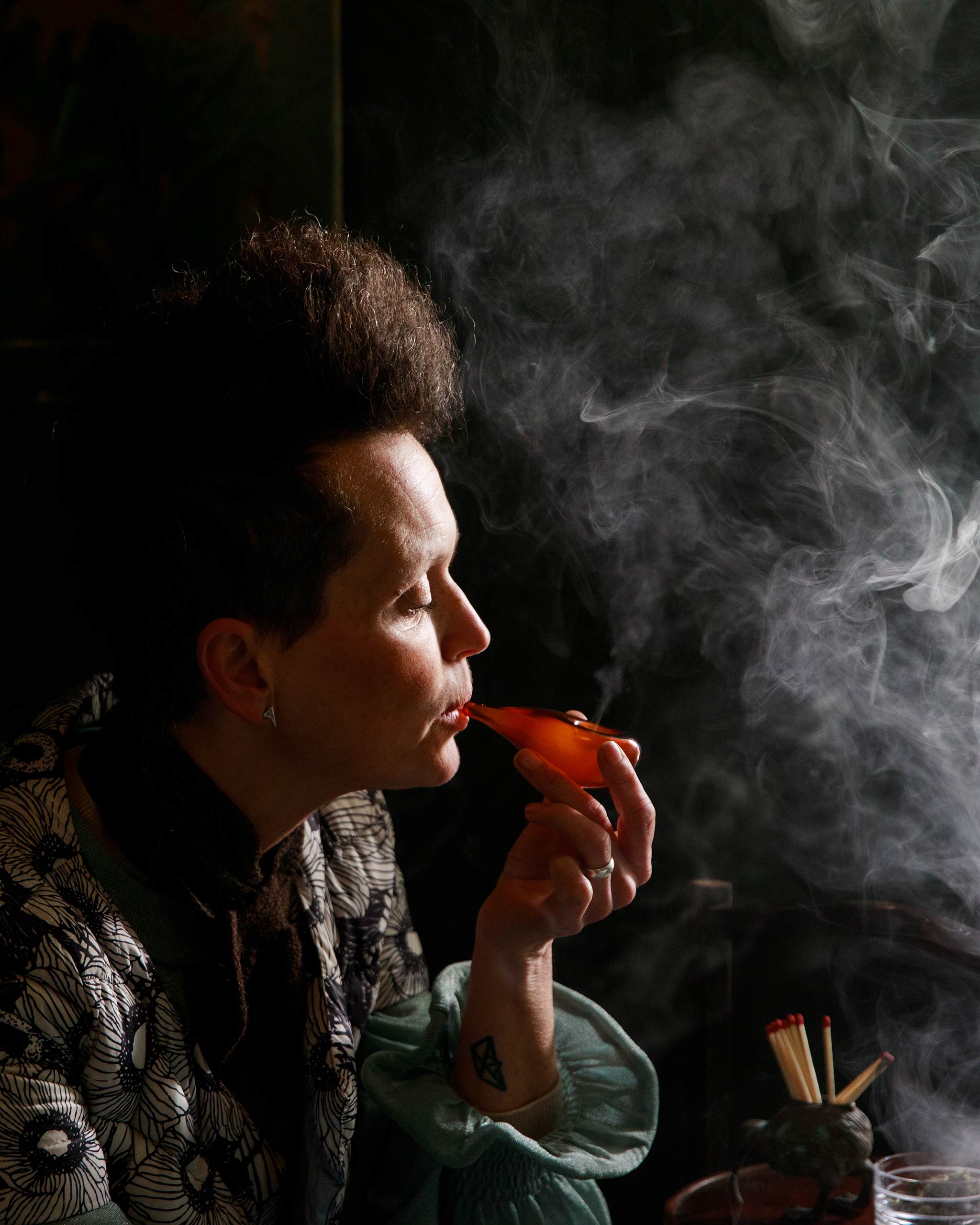 Woman smoking a mouth-blown glass Cloud Pipe, smoke drifting gently through a dark, atmospheric scene that highlights the sculptural elegance of the piece.