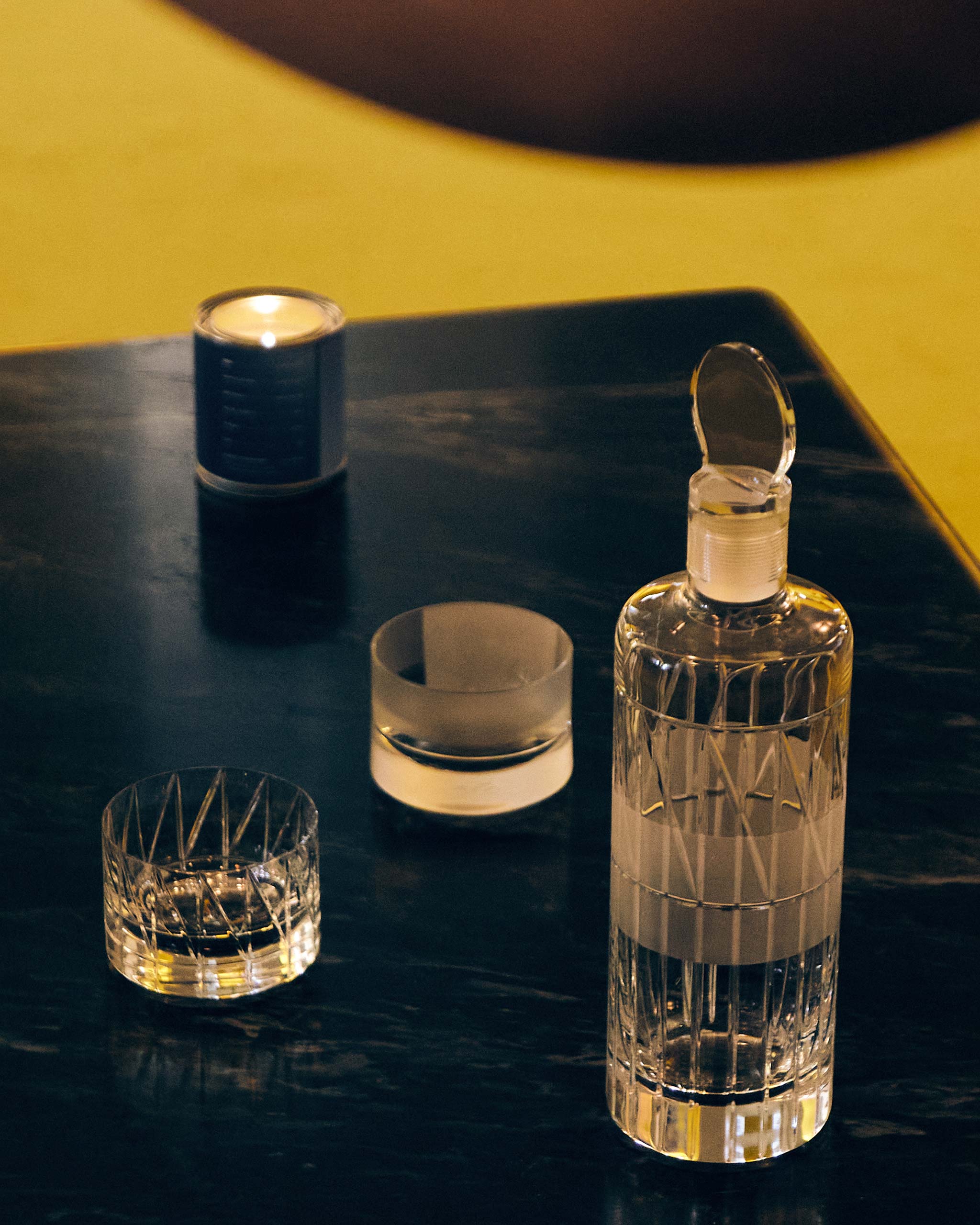 Hand-blown crystal whiskey decanter with stopper alongside two crystal low whiskey glasses on a marble tabletop.