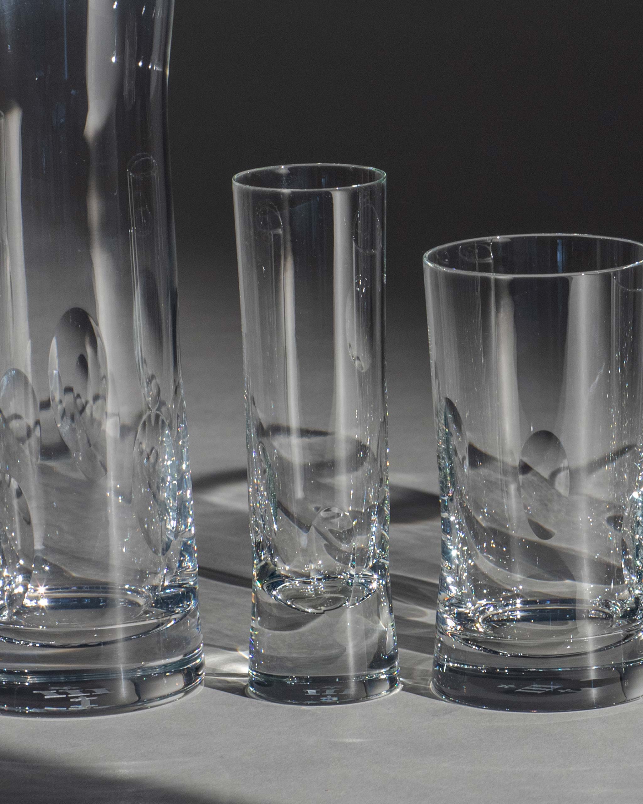 Polished hand-cut Irish crystal champagne flute with softly polished and sandblasted dew-cut detailing alongside other glassware on an ambient background