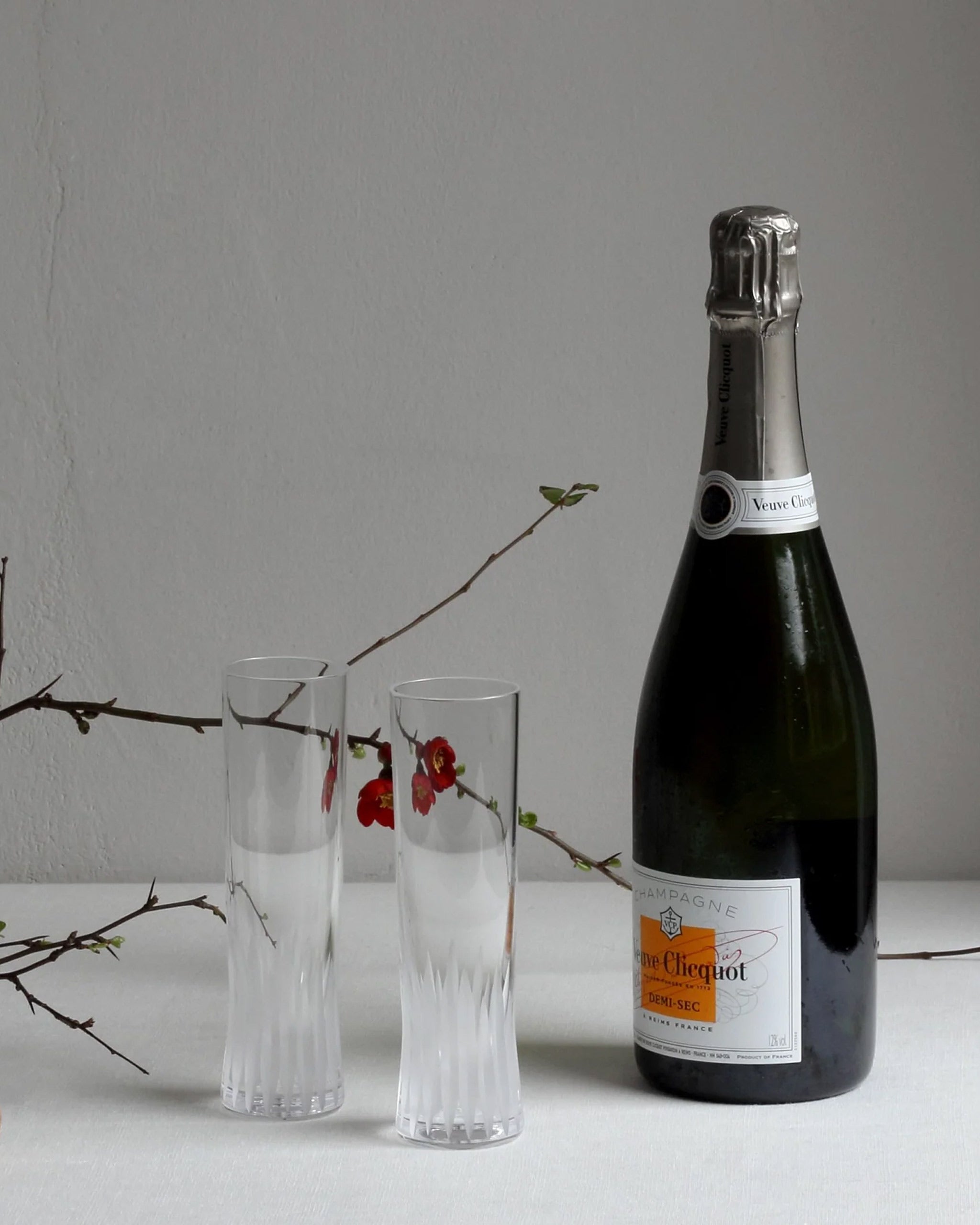 Lifestyle image of hand-cut Irish crystal champagne flutes alongside a champagne bottle and blossoming branch
