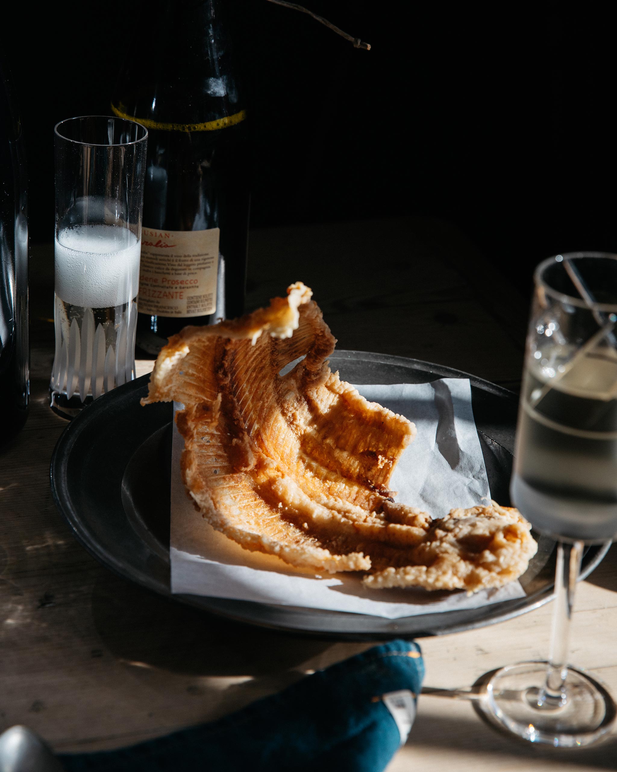 Festive dining table scene with a hand-blown cut crystal champagne flute, champagne bottle and a fish dish.