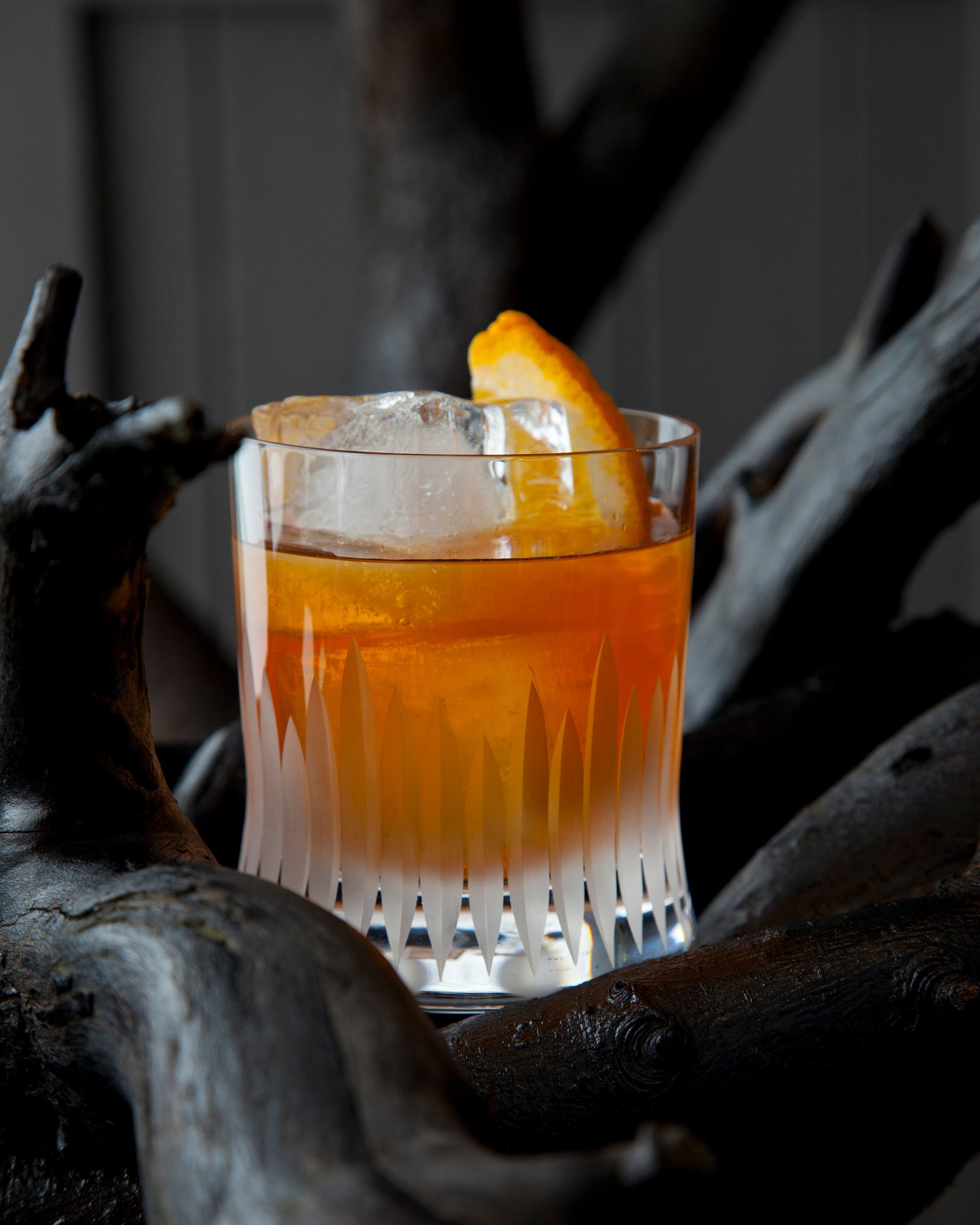 Unpolished hand-cut Irish crystal whiskey glass filled with an orange cocktail, ice cube and orange rind garnish.