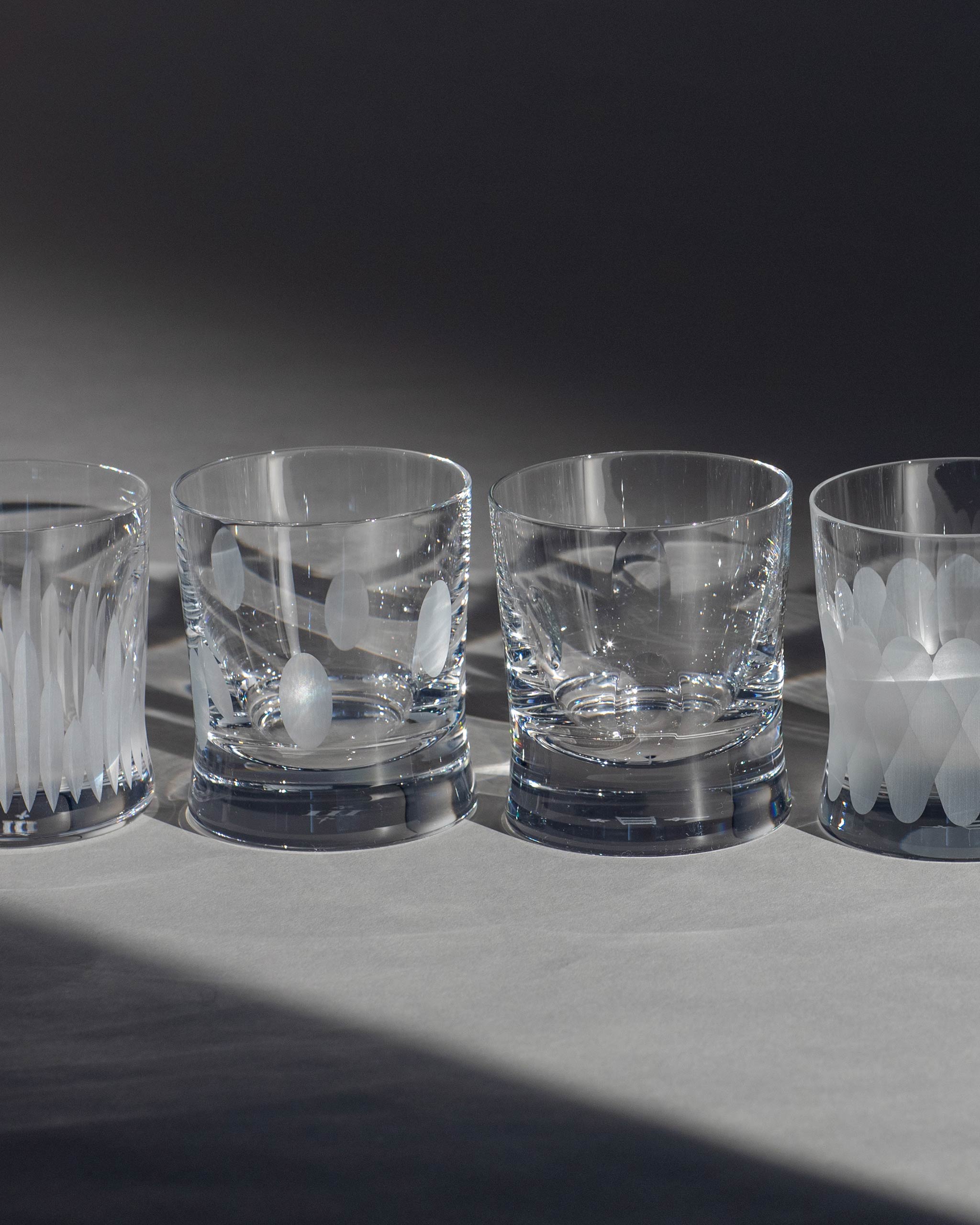 Array of hand-cut Irish crystal whiskey low glasses with softly polished and sandblasted detailing on an ambient background