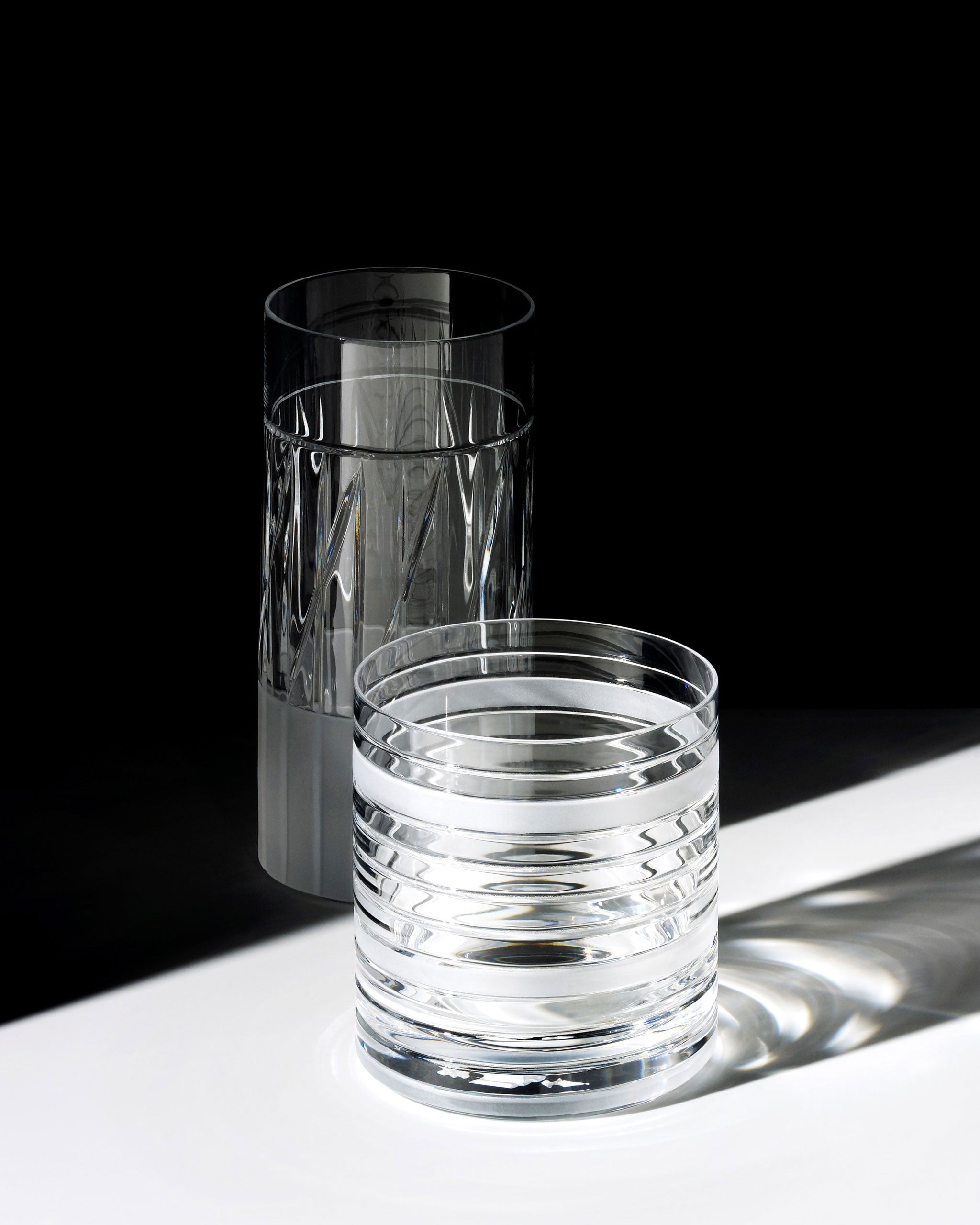 Handcrafted crystal tumbler and highball glass, both showcasing sharp linear cuts and sculptural design
