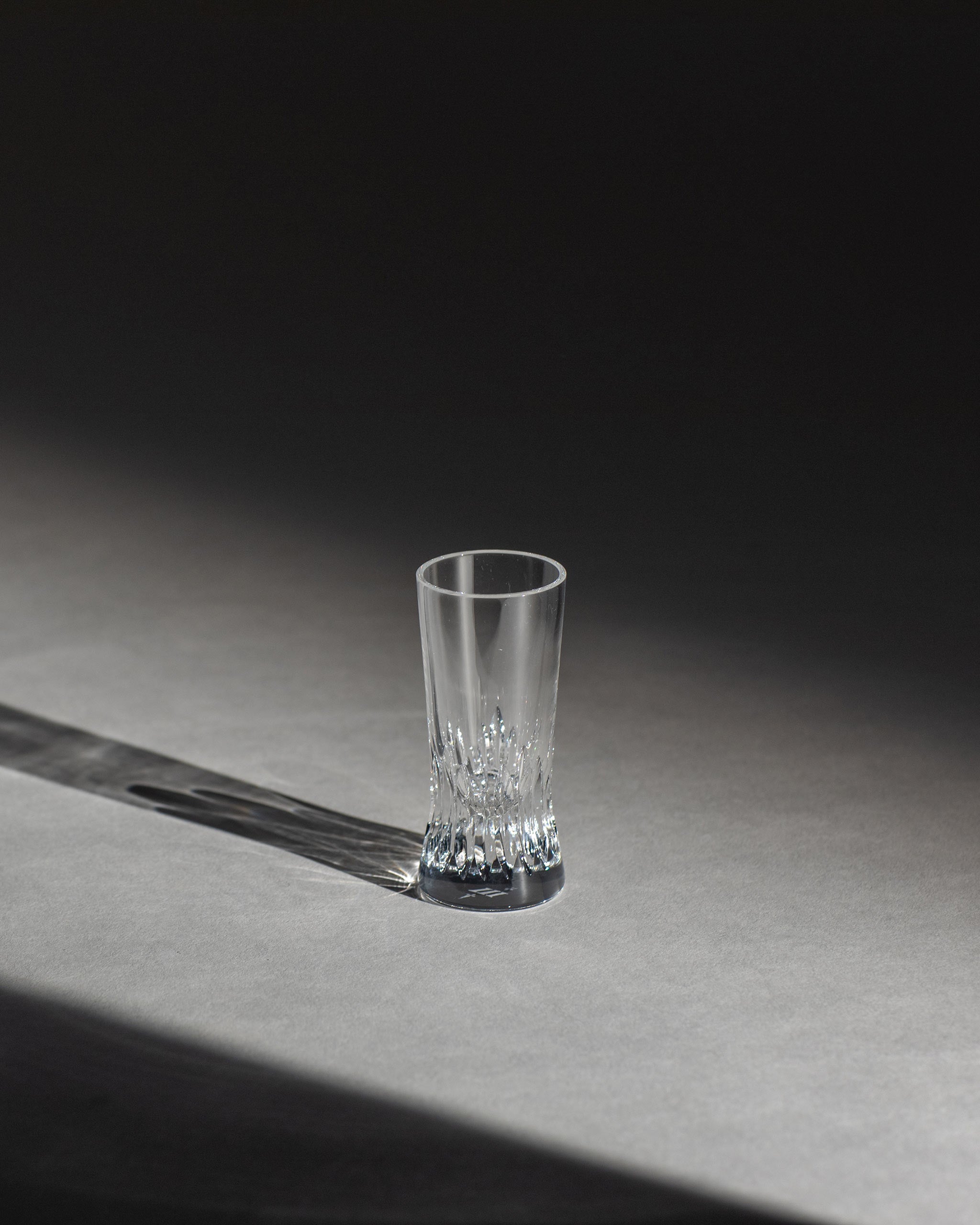 Polished hand-cut Irish crystal shot glass with deep angular cuts inspired by ploughed soil on an ambient background