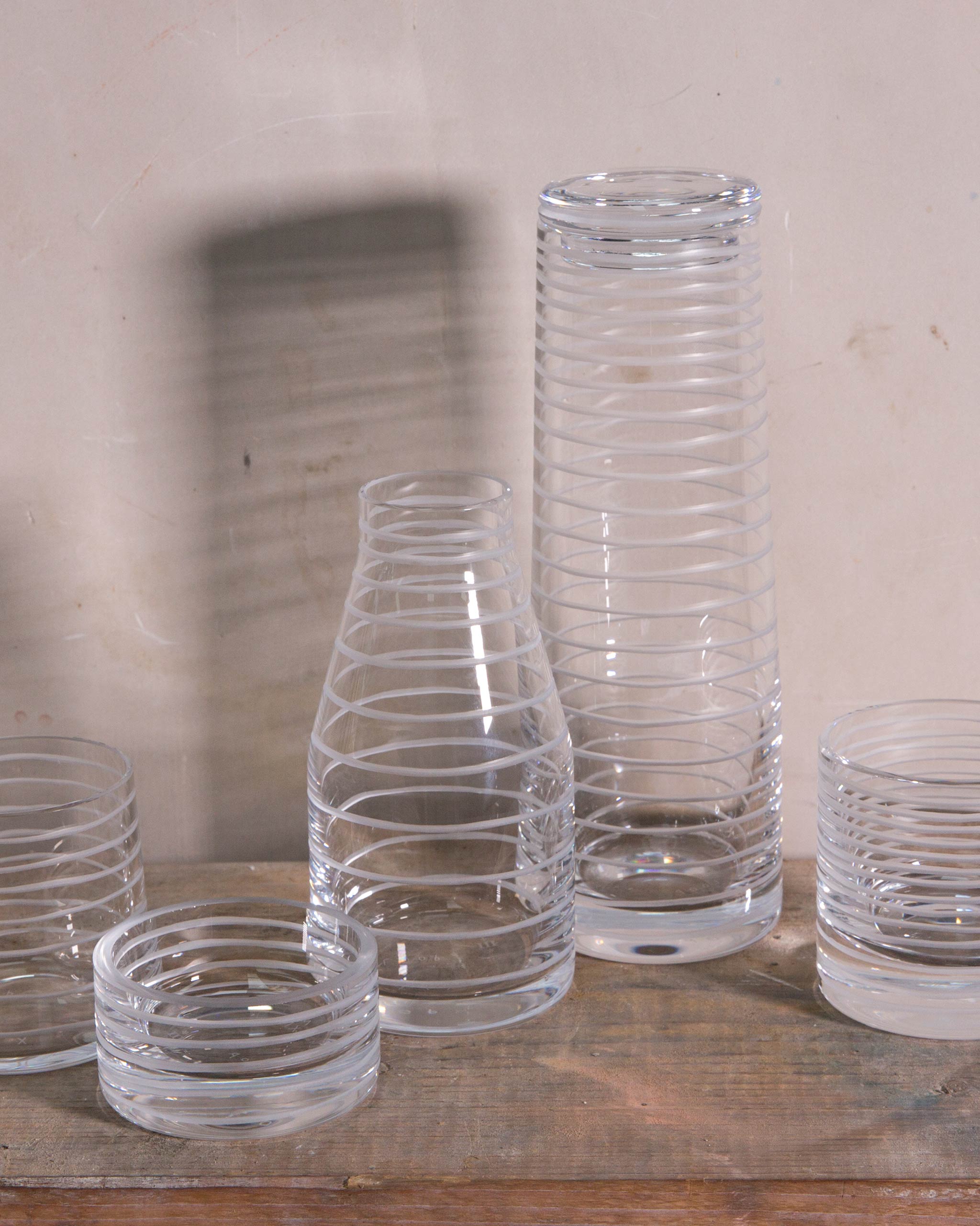 Complete Loop Collection set of hand-cut Irish crystal tumblers, carafe, decanter, and votives displayed together on a natural wooden surface, highlighting vertical cut design and symmetry.