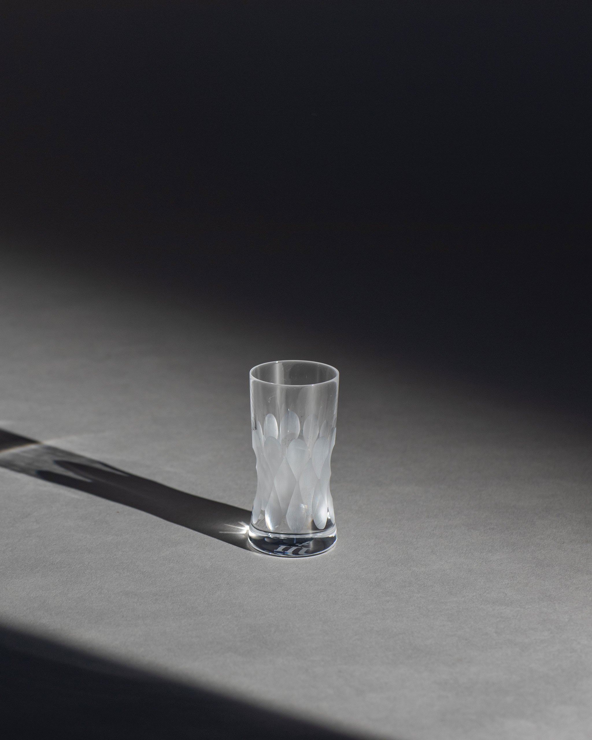 Unpolished Irish hand-blown cut crystal shot or grappa glass with large cut pattern detailing on an ambient background