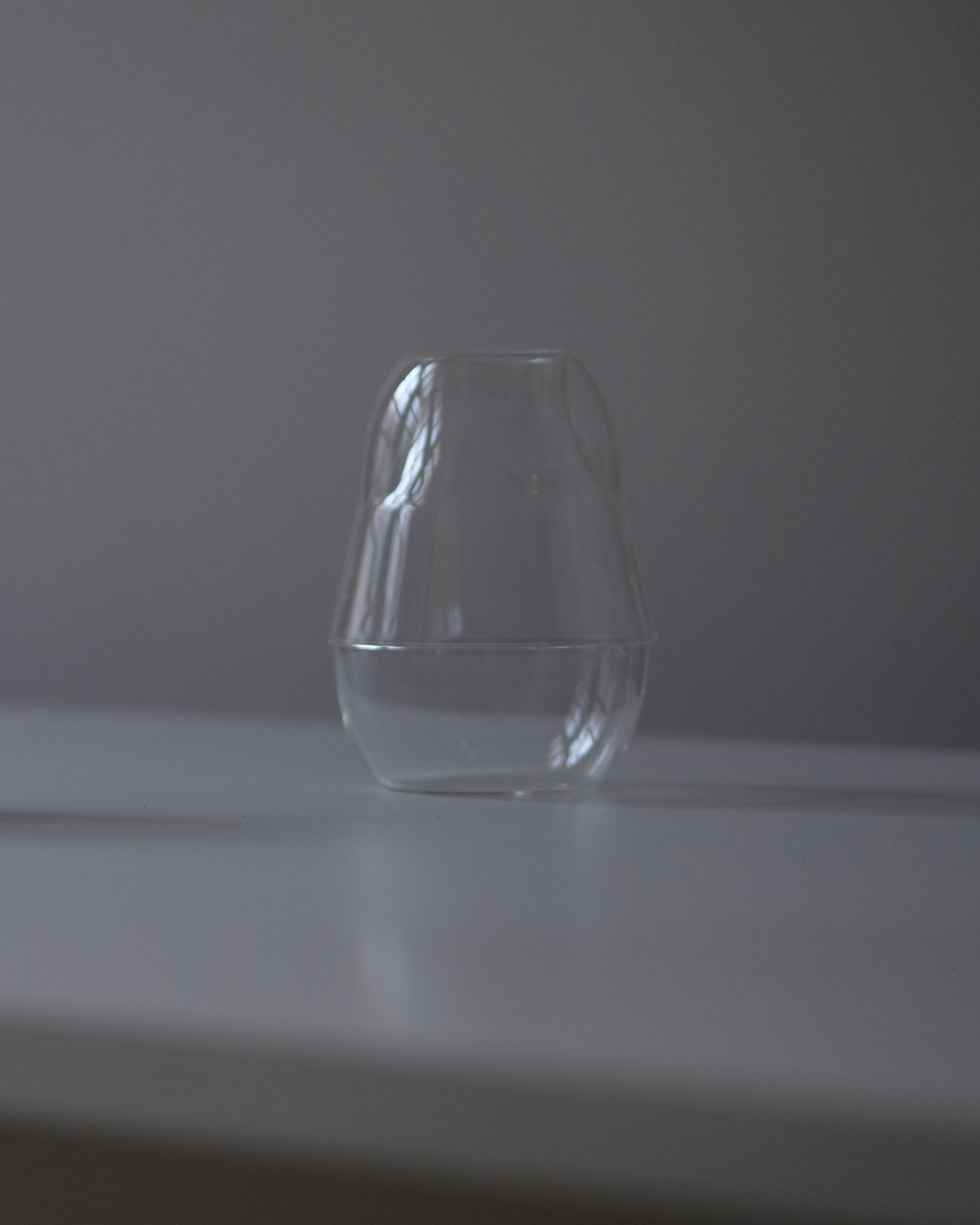 Clear borosilicate glass carafe with matching drinking glass stacked neatly on top, forming a unified closed unit, on a dark grey tabletop.