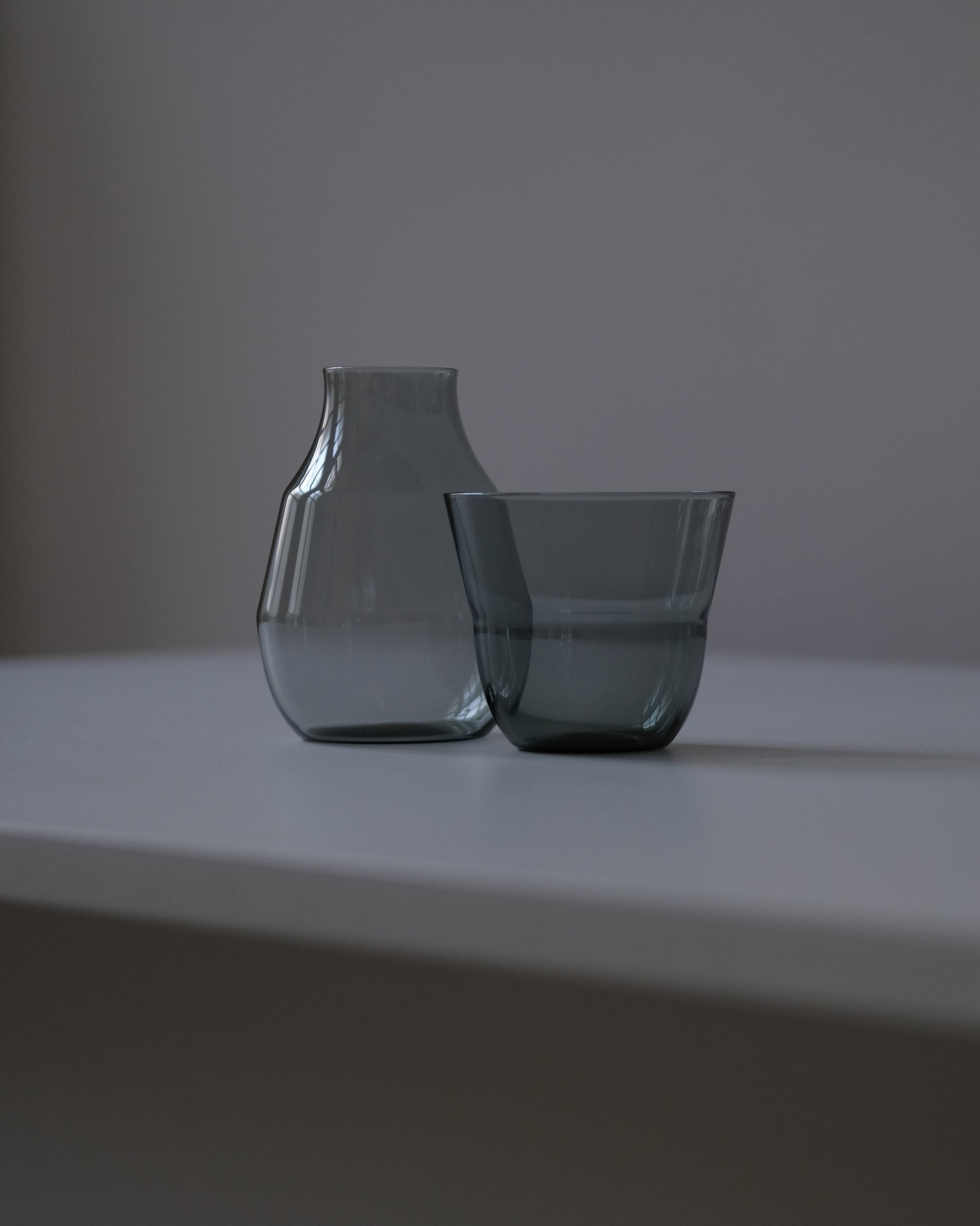 Grey borosilicate glass carafe and tumbler set shown side by side on a dark grey surface for a tonal, modern look.
