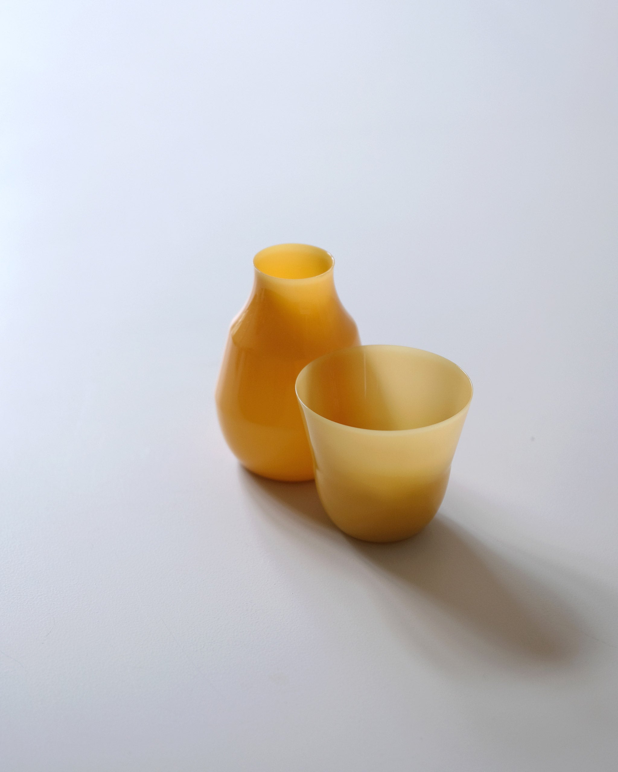 Ochre mouth-blown borosilicate glass carafe and matching glass designed by displayed side by side on a white table.