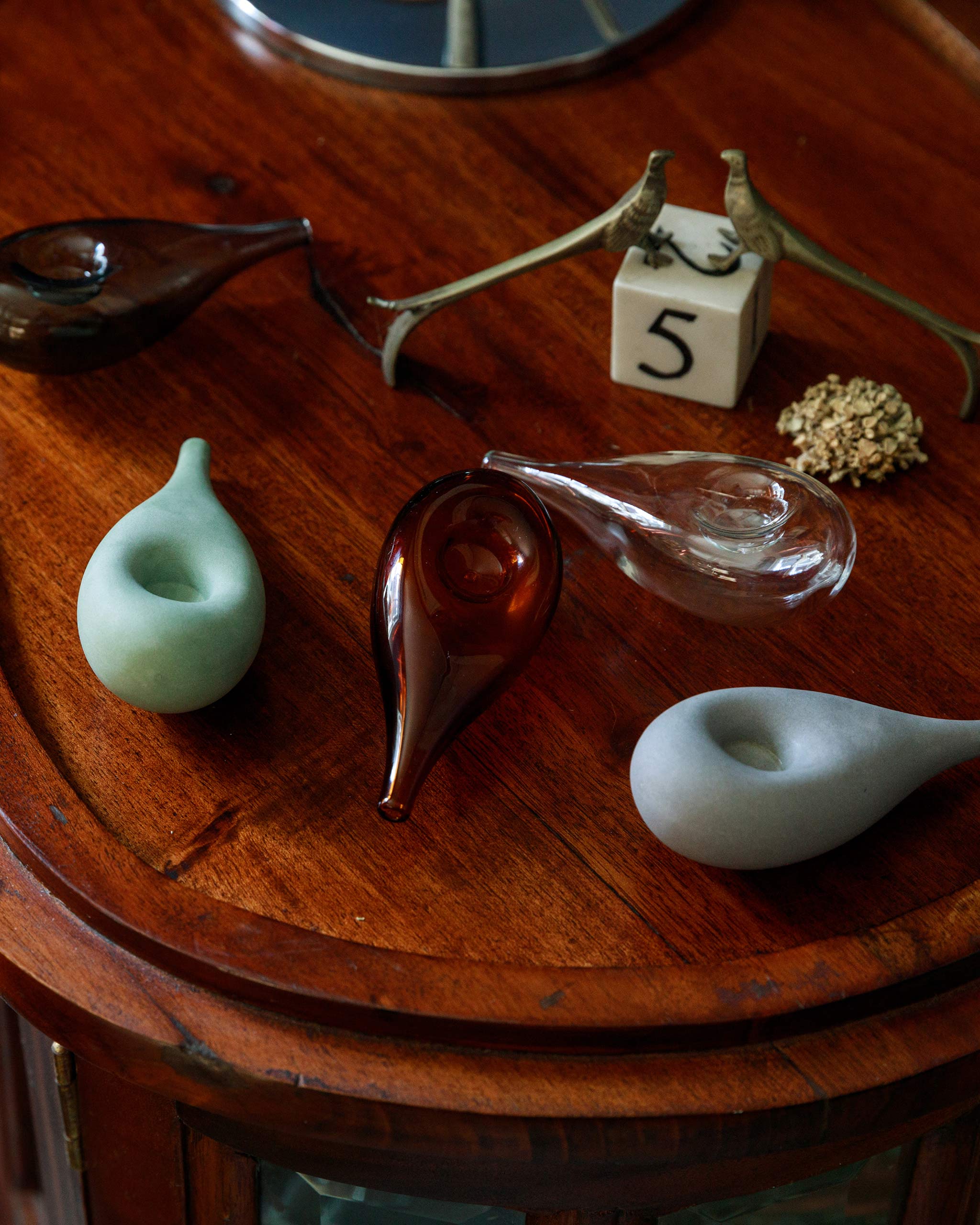 Collection of Cloud Pipes in porcelain and glass on a wooden table with a dice and small trinkets, creating a warm, intimate lifestyle composition.