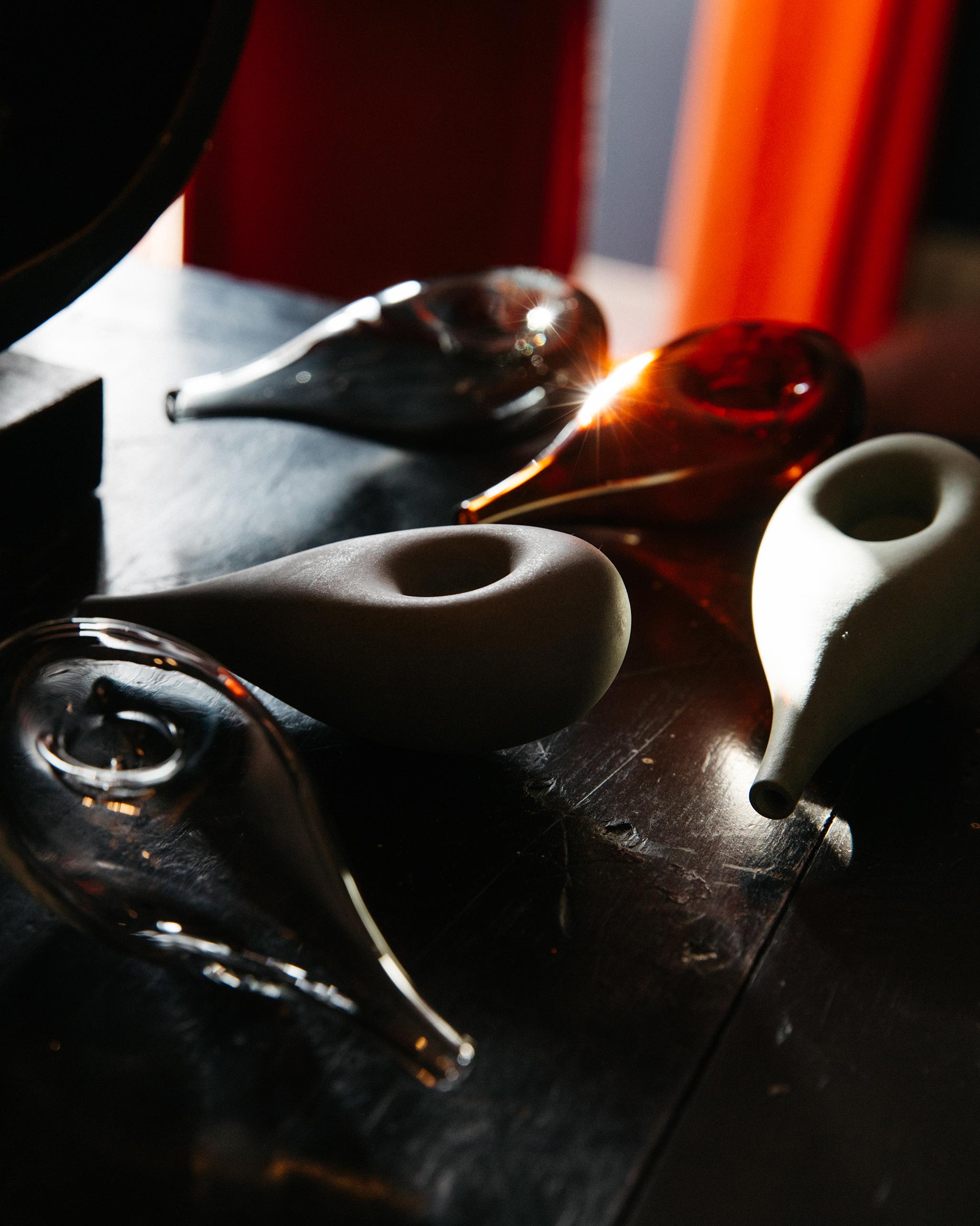 Five Cloud Pipes in glass and porcelain on a wooden table, illuminated by soft daylight filtering through curtains, showcasing form, material, and transparency.