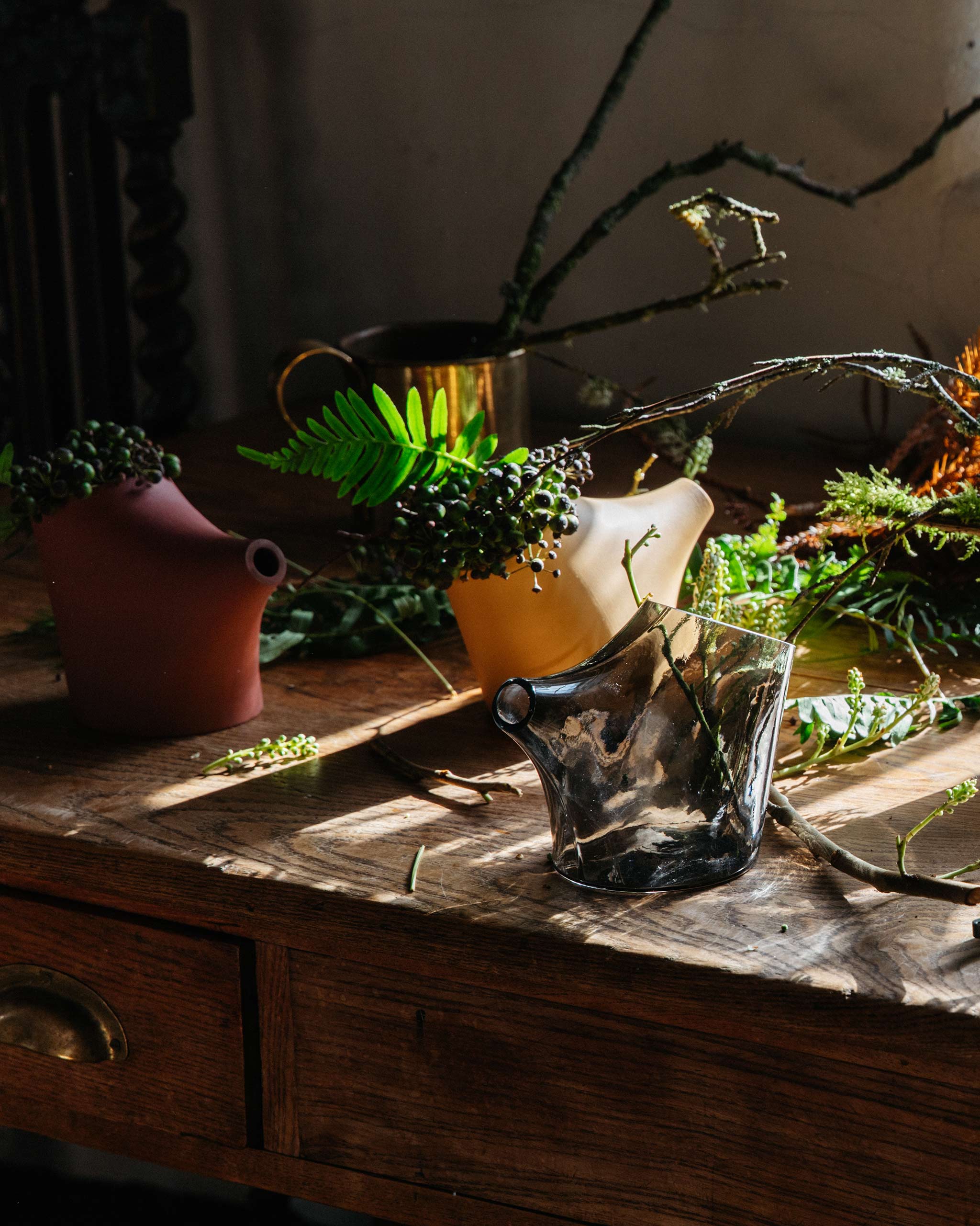 Kiln-cast HopStep pots on a warmly lit table, with light filtering through the translucent forms and foliage inside.