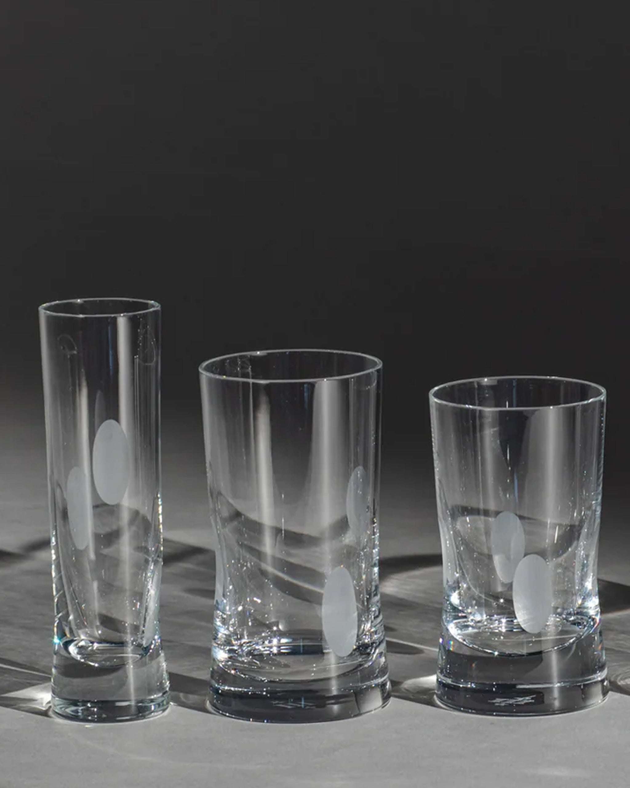 Unpolished hand-cut Irish crystal champagne flute with softly polished and sandblasted dew-cut detailing alongside other glassware on an ambient background