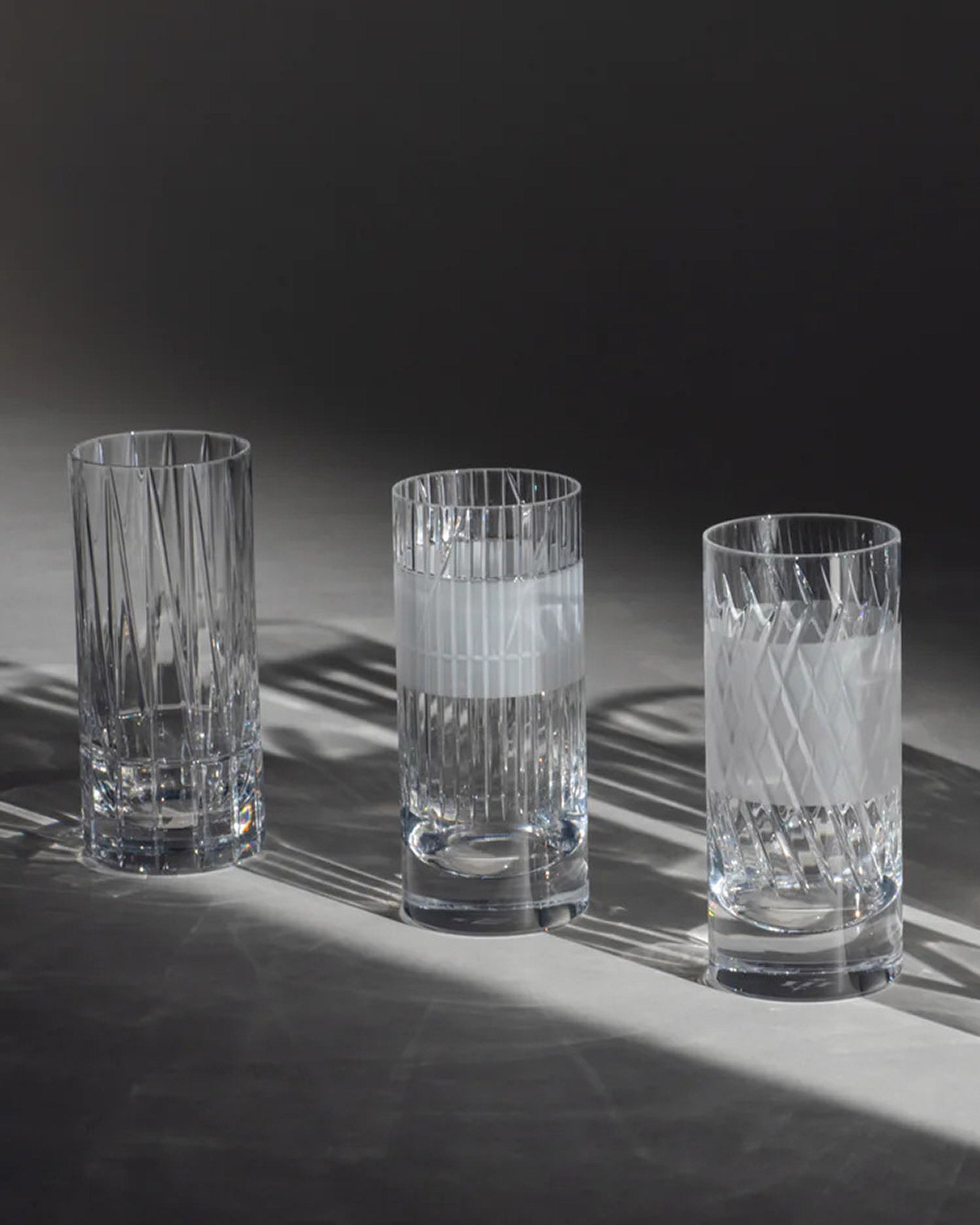 A trio of tall cut crystal long highball glasses showcasing cut crystal and frosted detailing against an ambient background