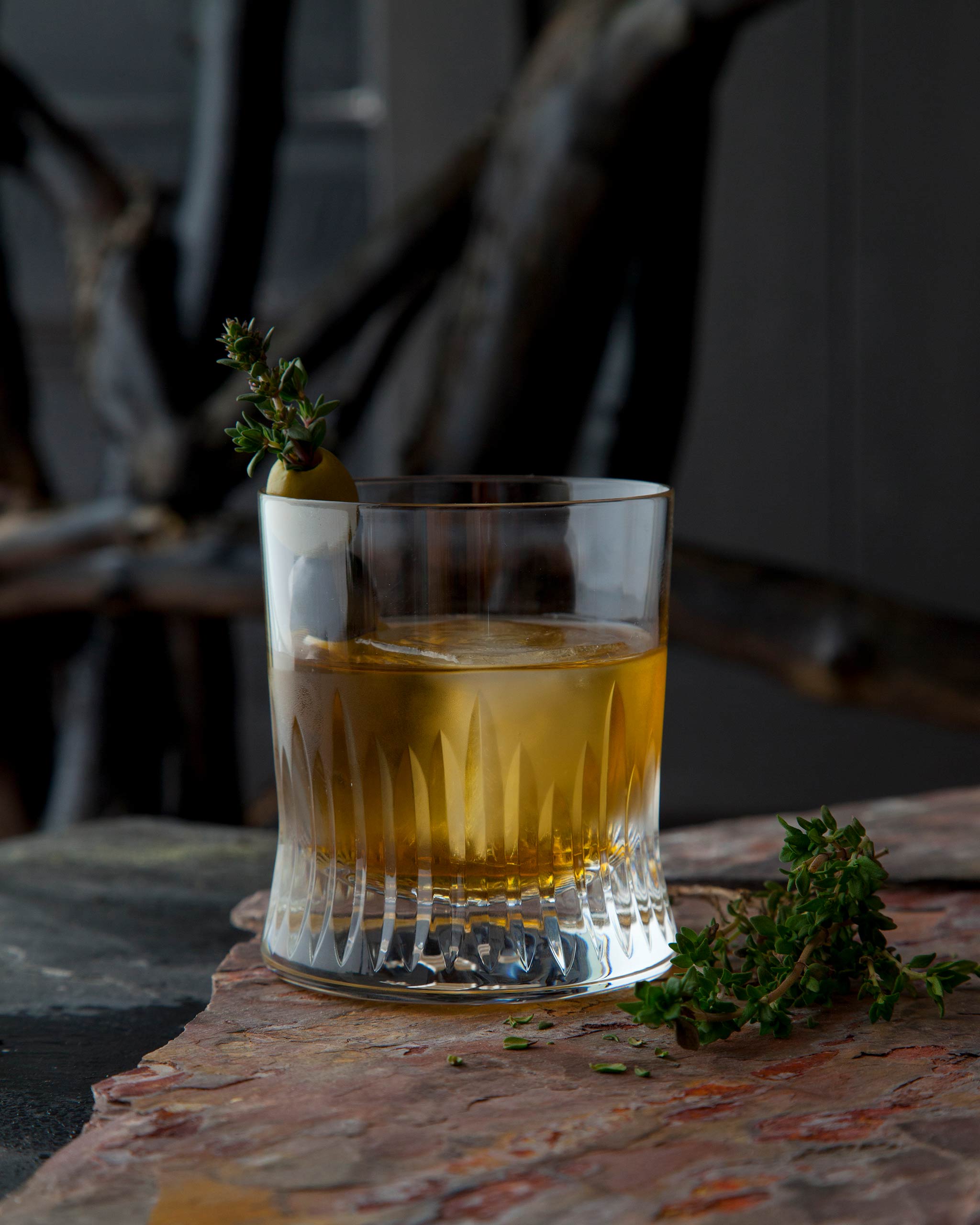 Unpolished hand-cut Irish crystal whiskey glass filled with whiskey cocktail, ice cube and olive granish