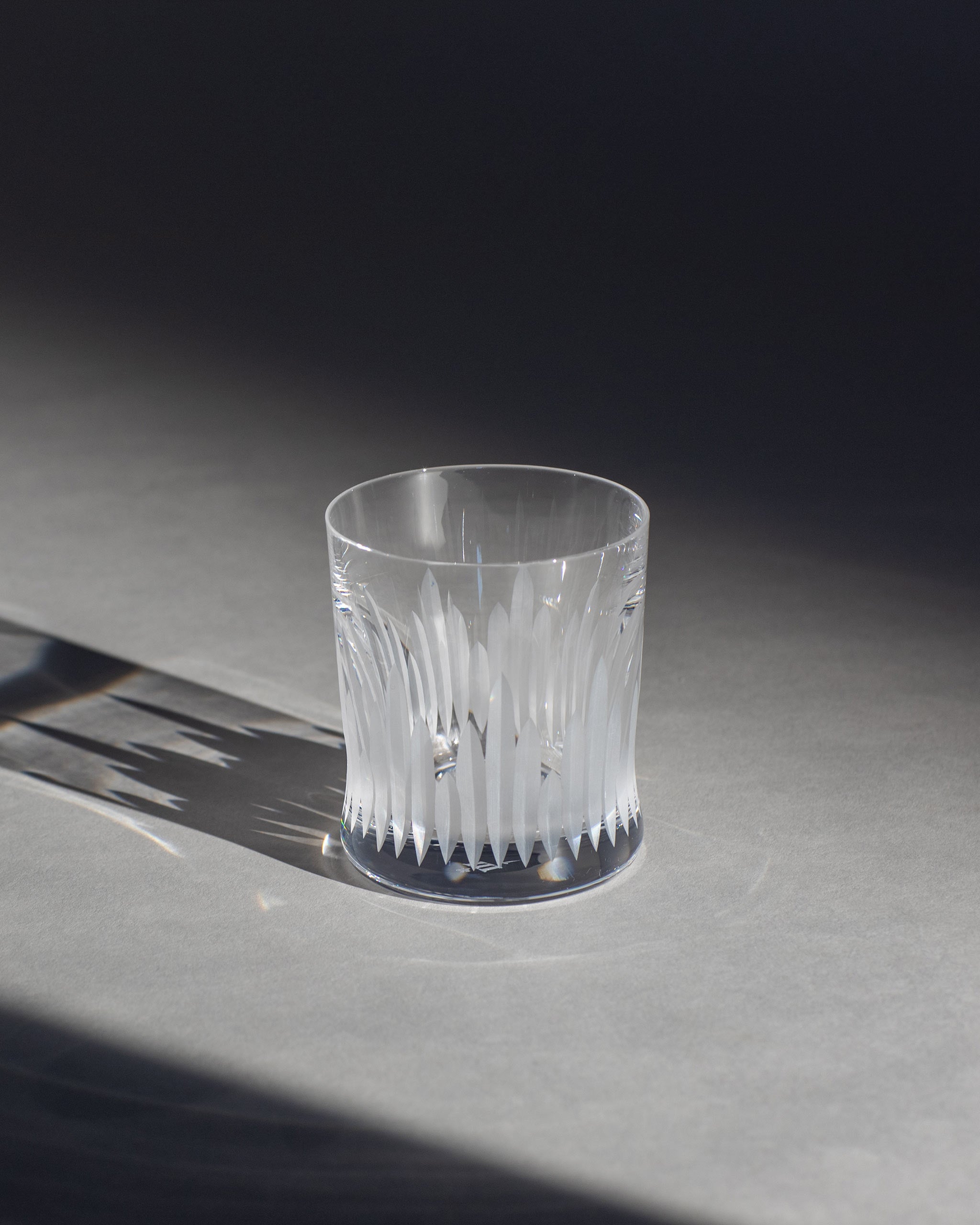 Unpolished hand-cut Irish crystal whiskey glass with deep angular cuts inspired by ploughed soil on an ambient background