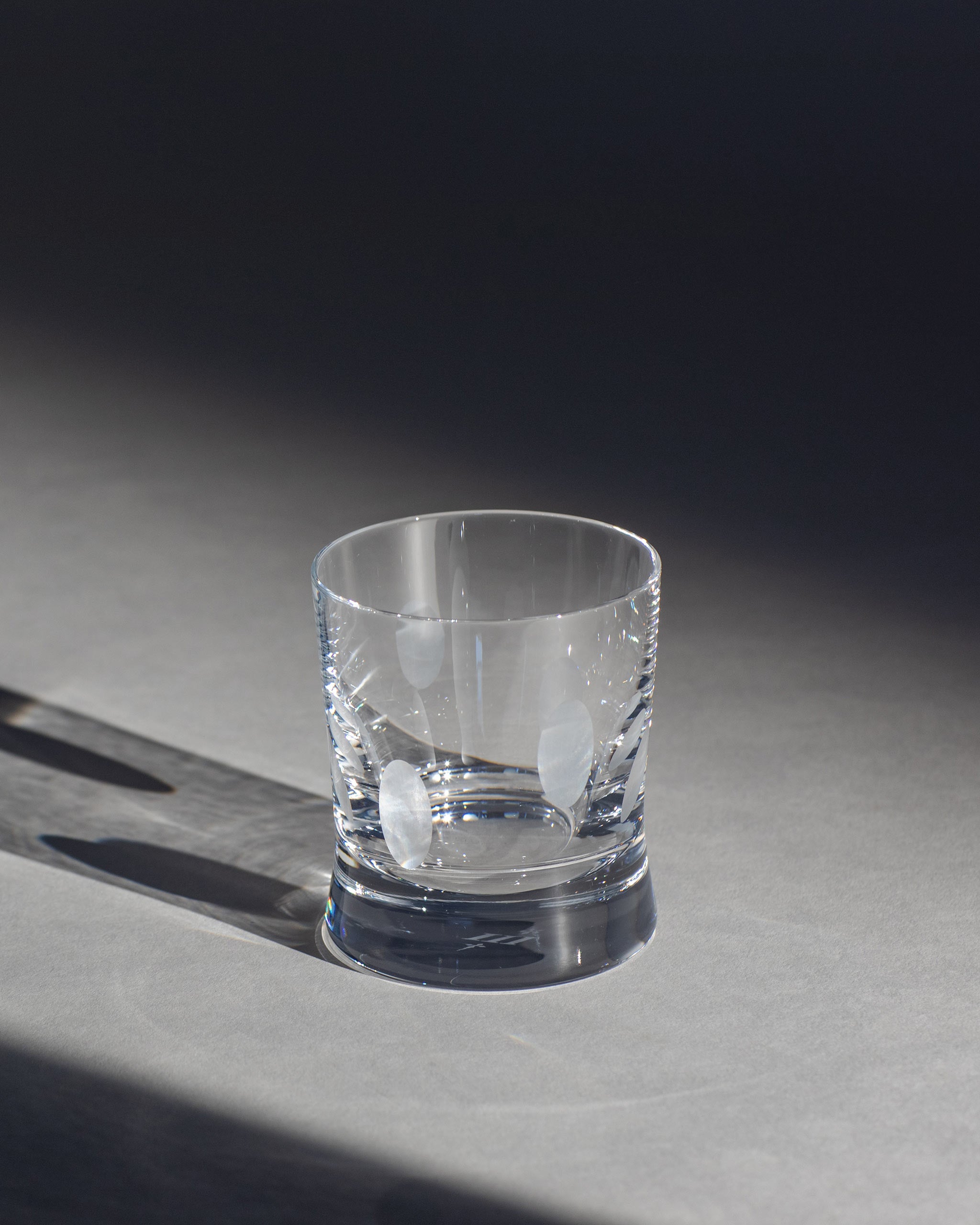 Unpolished hand-cut Irish crystal whiskey low glass with softly polished and sandblasted dew-cut detailing on an ambient background