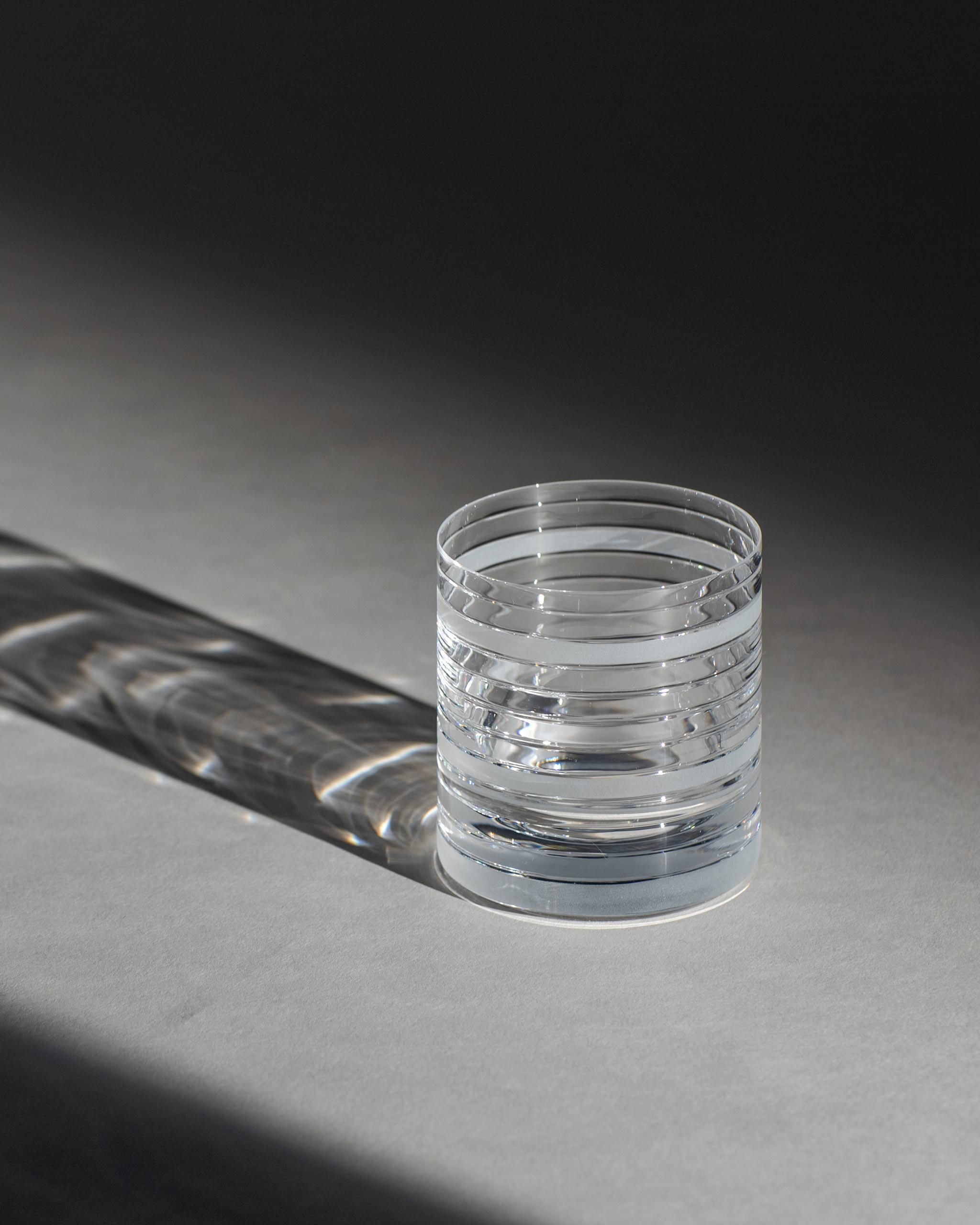 Handcrafted crystal tumbler with sharp horizontal cuts and sculptural design against an ambient background