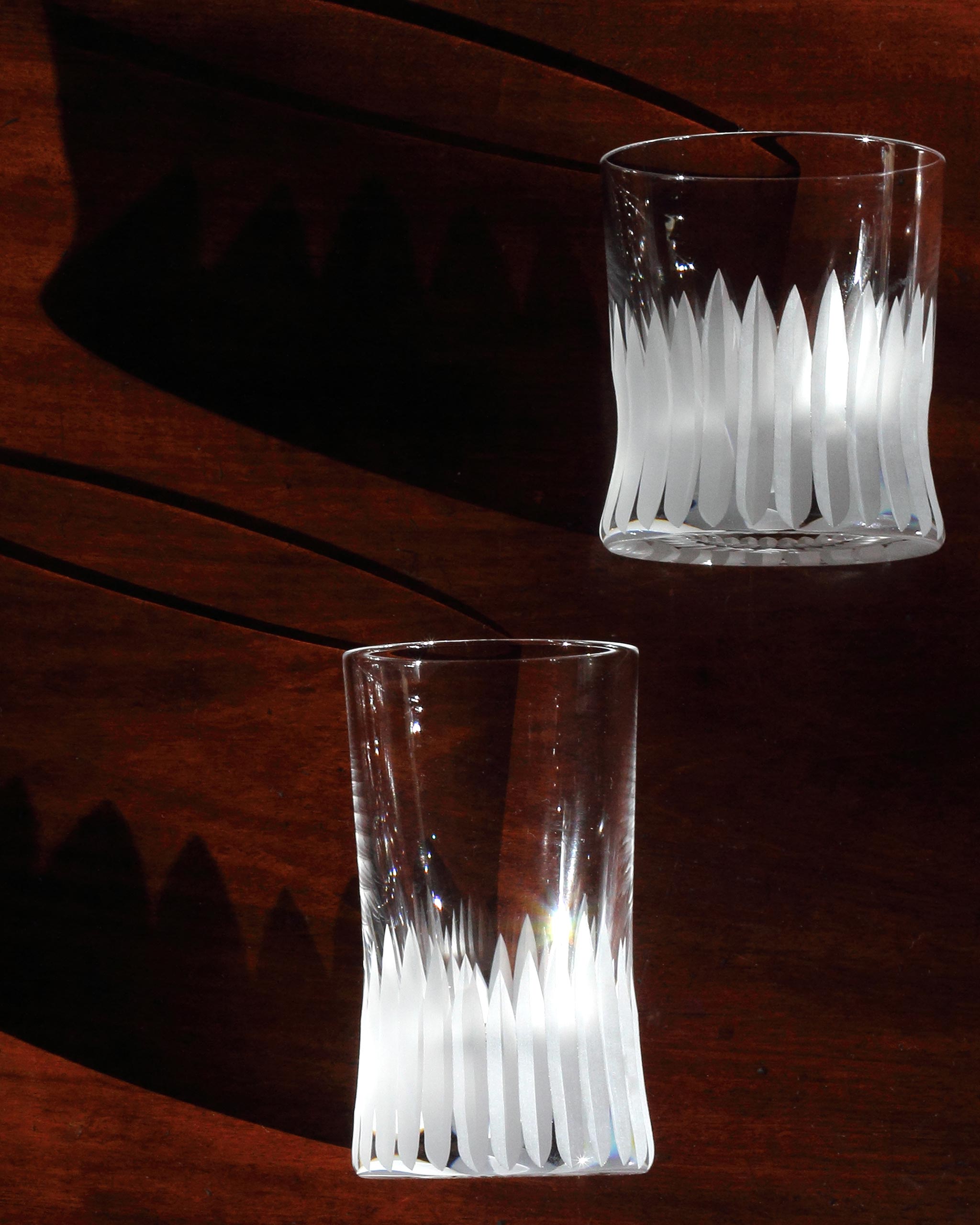 Duo of hand-blown cut crystal glasses warmly lit to highlight distinct deep cut detailing, against a wooden table