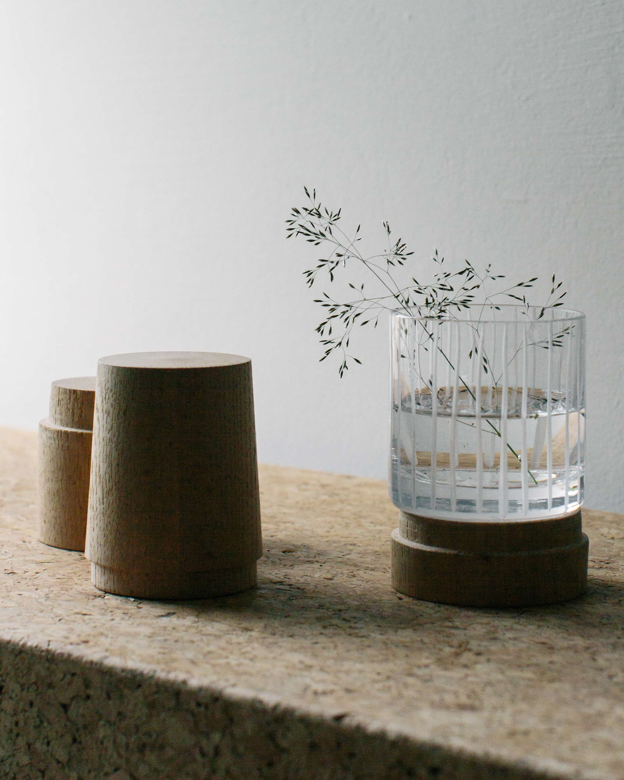 Hand-cut Irish crystal Row Collection straight tumbler filled with water and soft plant, accompanied by cork objects, styled on a natural lifestyle surface.