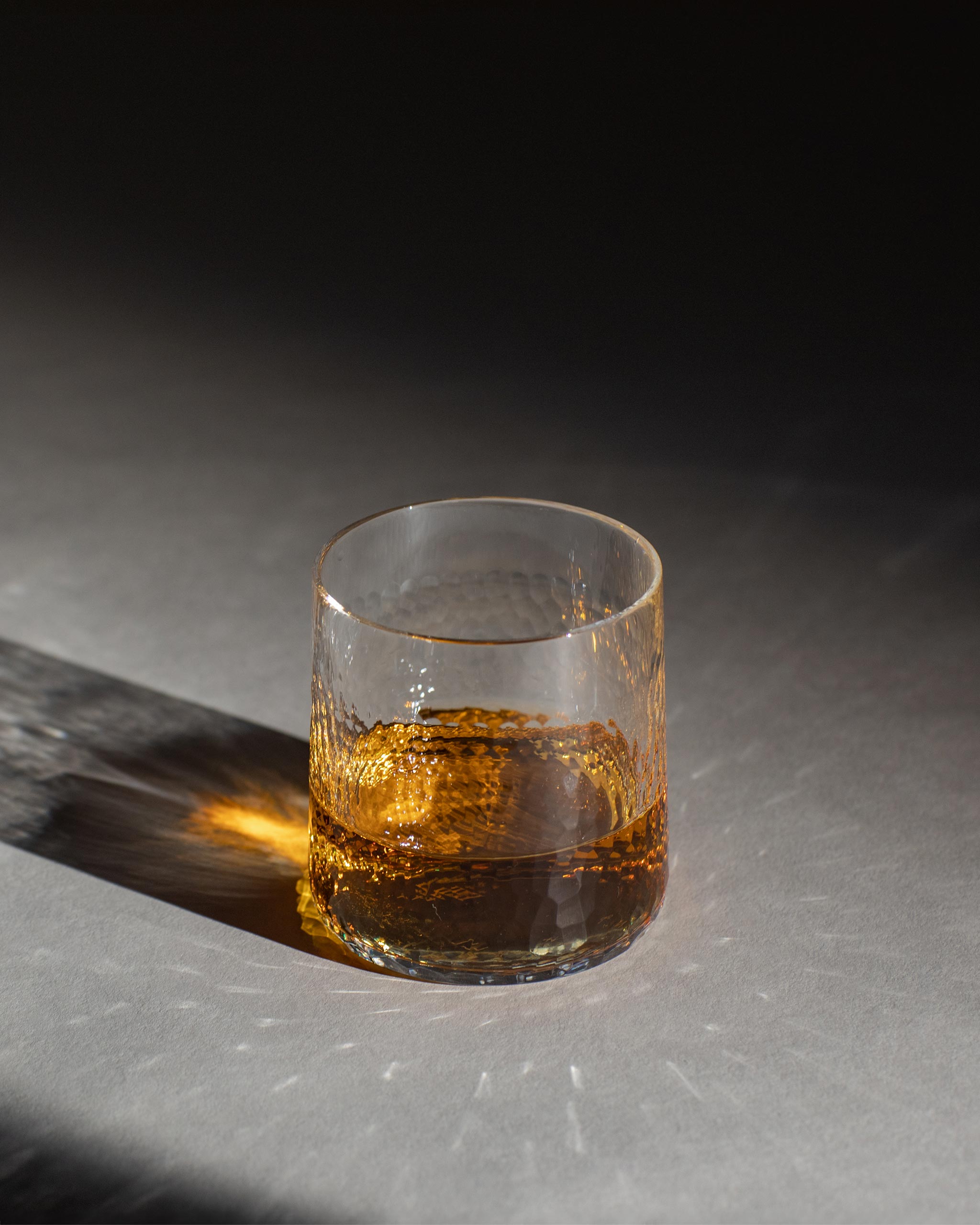 Polished straight tumbler in hand-cut Irish crystal filled with amber whiskey, displayed on a shadowy background highlighting refraction and texture.