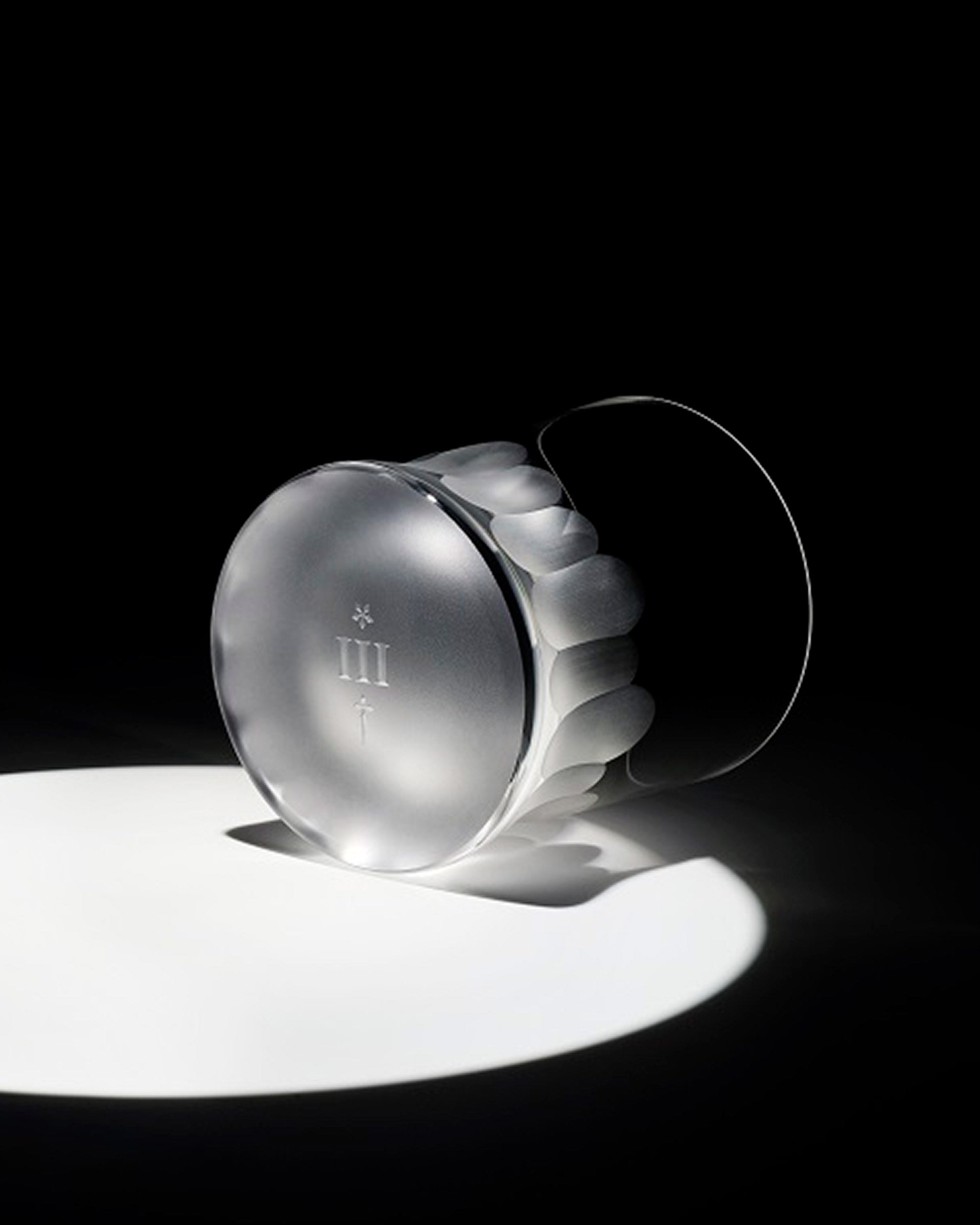 Hand-blown Irish crystal whiskey glass lying on its side, showcasing engraved branding on the base and unpolished cut detailing.