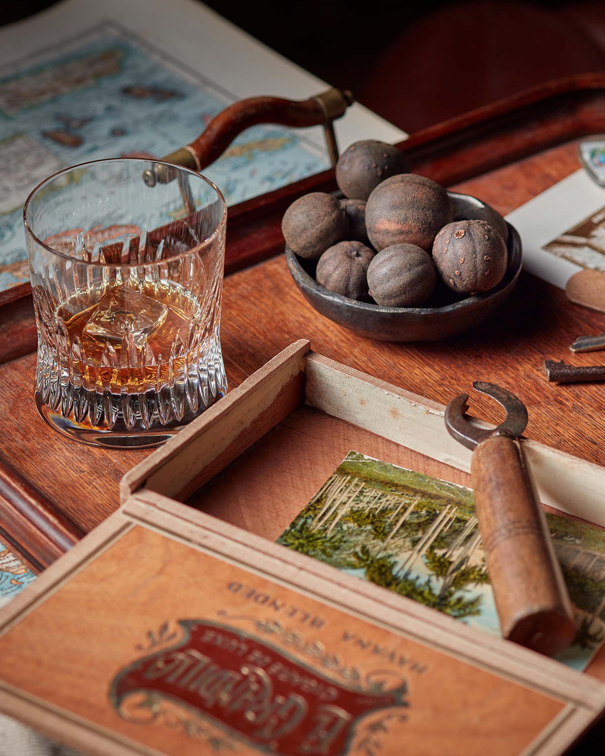 Hand-blown Irish crystal whiskey glass on a wooden desk with maps, walnuts, and a nutcracker, creating a warm lifestyle scene that evokes craftsmanship and heritage