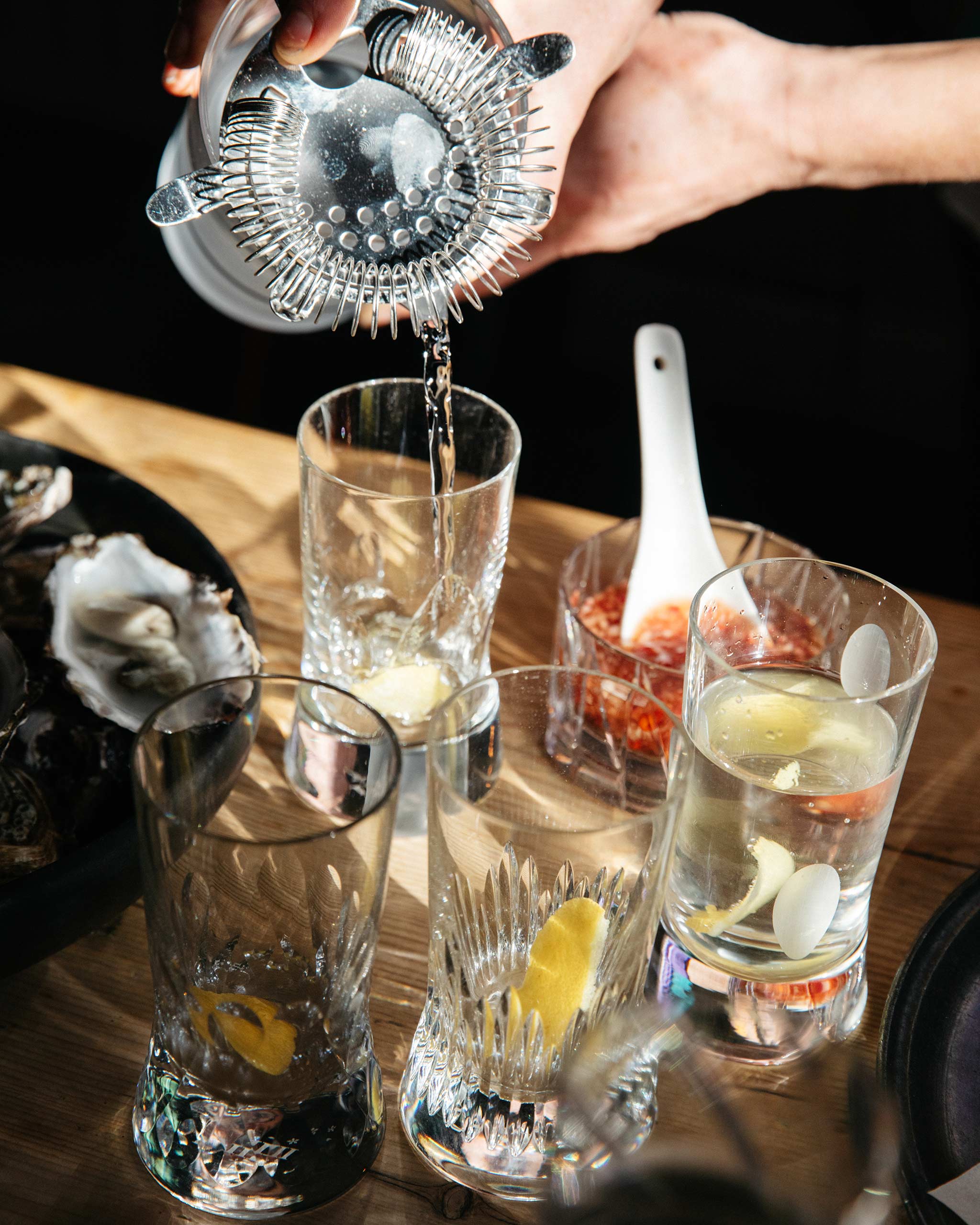 Elegant bar scene featuring hand-cut crystal wine glasses being used for cocktails, a shaker pouring drinks, and oysters on the table.