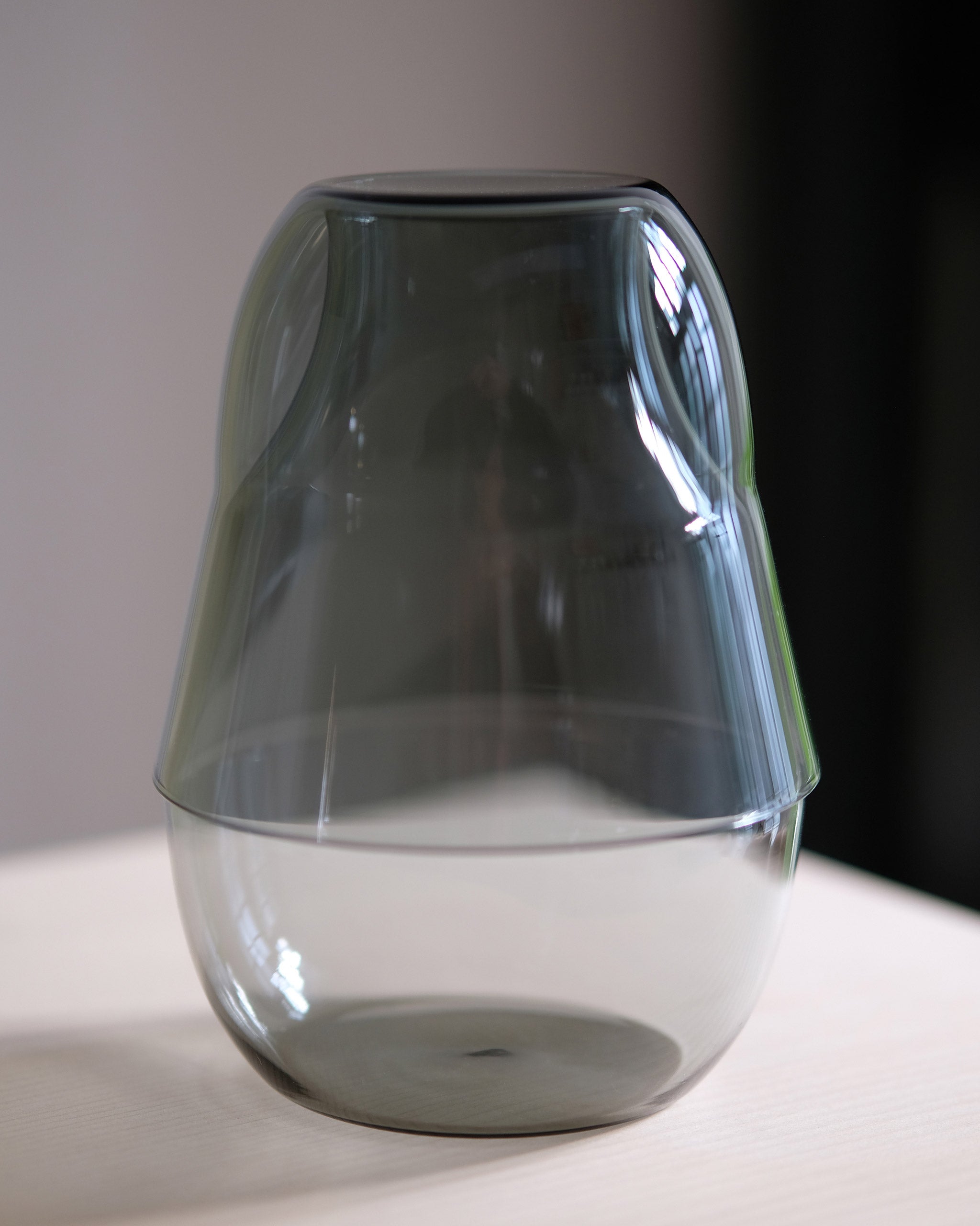 Close-up of grey mouth-blown borosilicate glass carafe and glass stacked together as a single sculptural unit, showcasing refined craftsmanship and minimalist form.