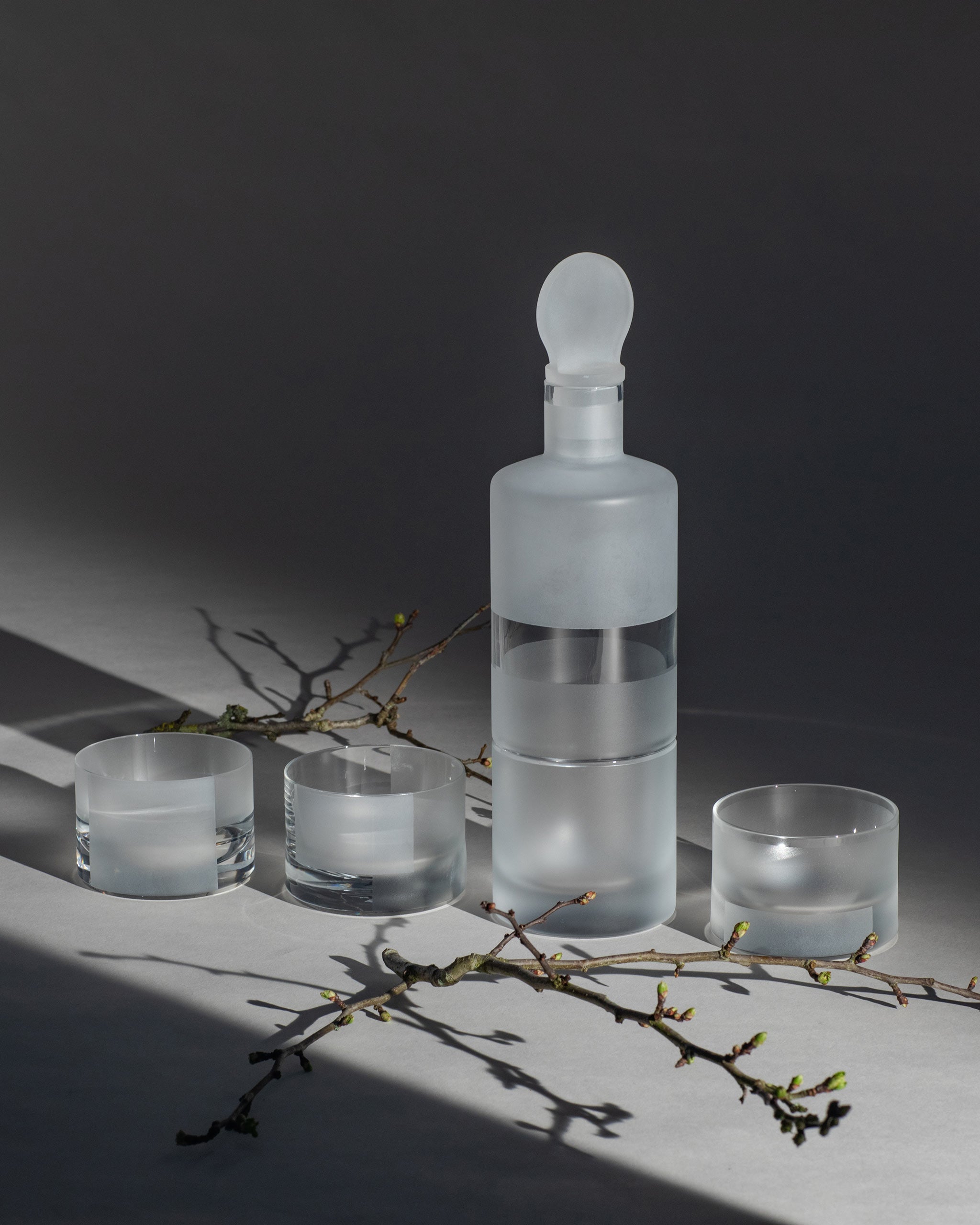 Crystal low drink glasses placed beside crystal whiskey decanter and birch branches.