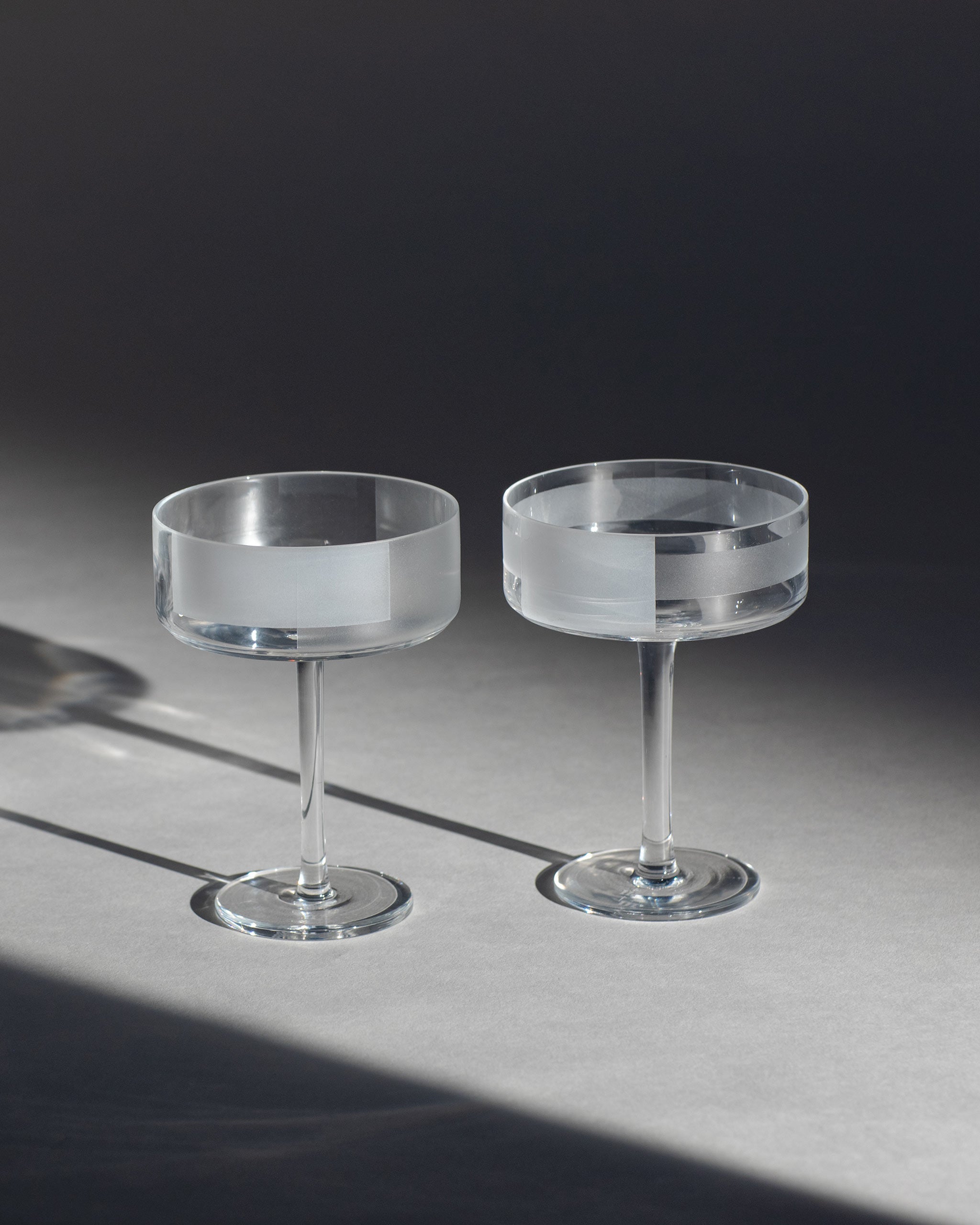 Two crystal cocktail coupe with half-frosted geometric design sit on an ambient background.