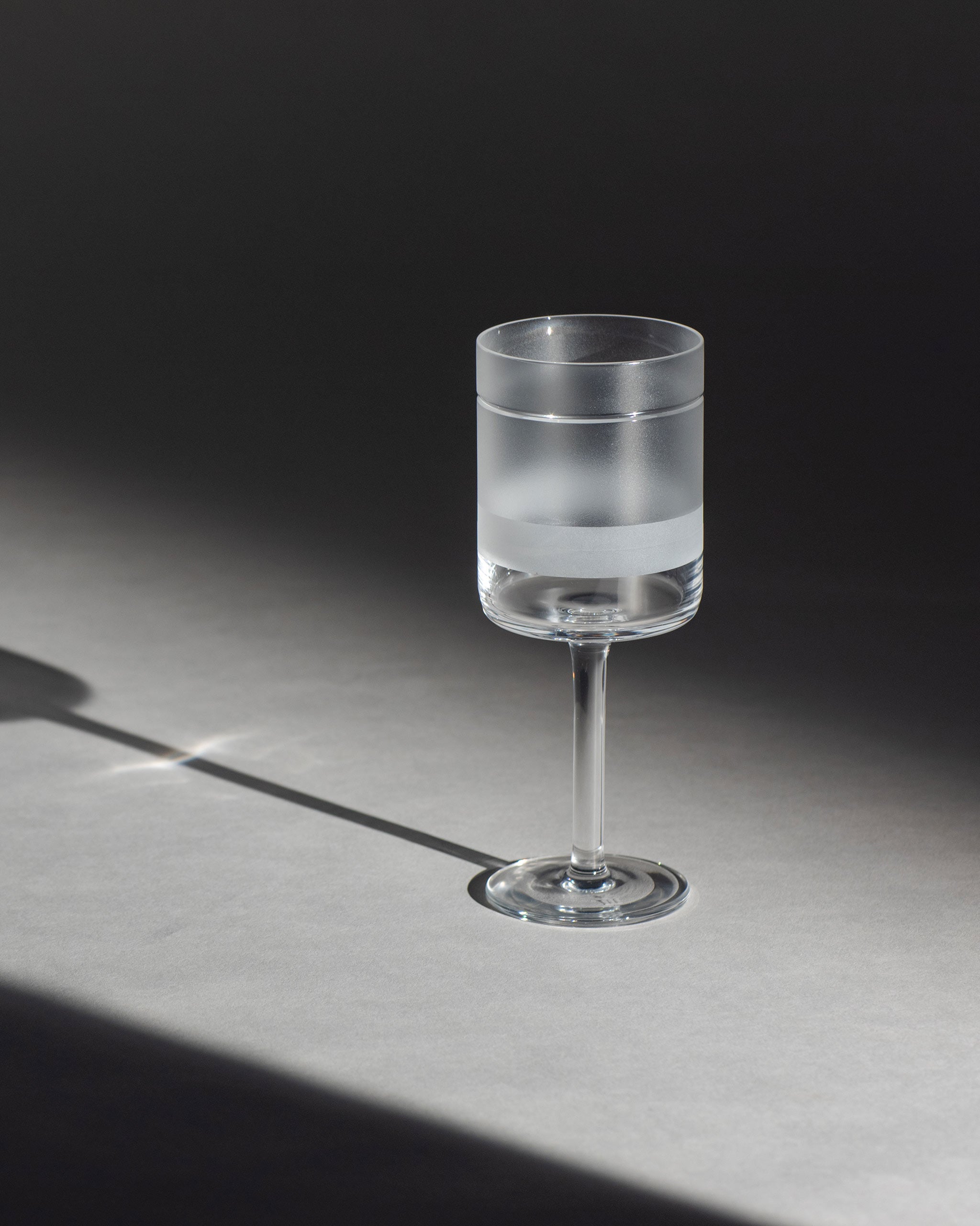 Elegant crystal red wine glass with sandblasted geometric panels and linear cuts against an ambient background