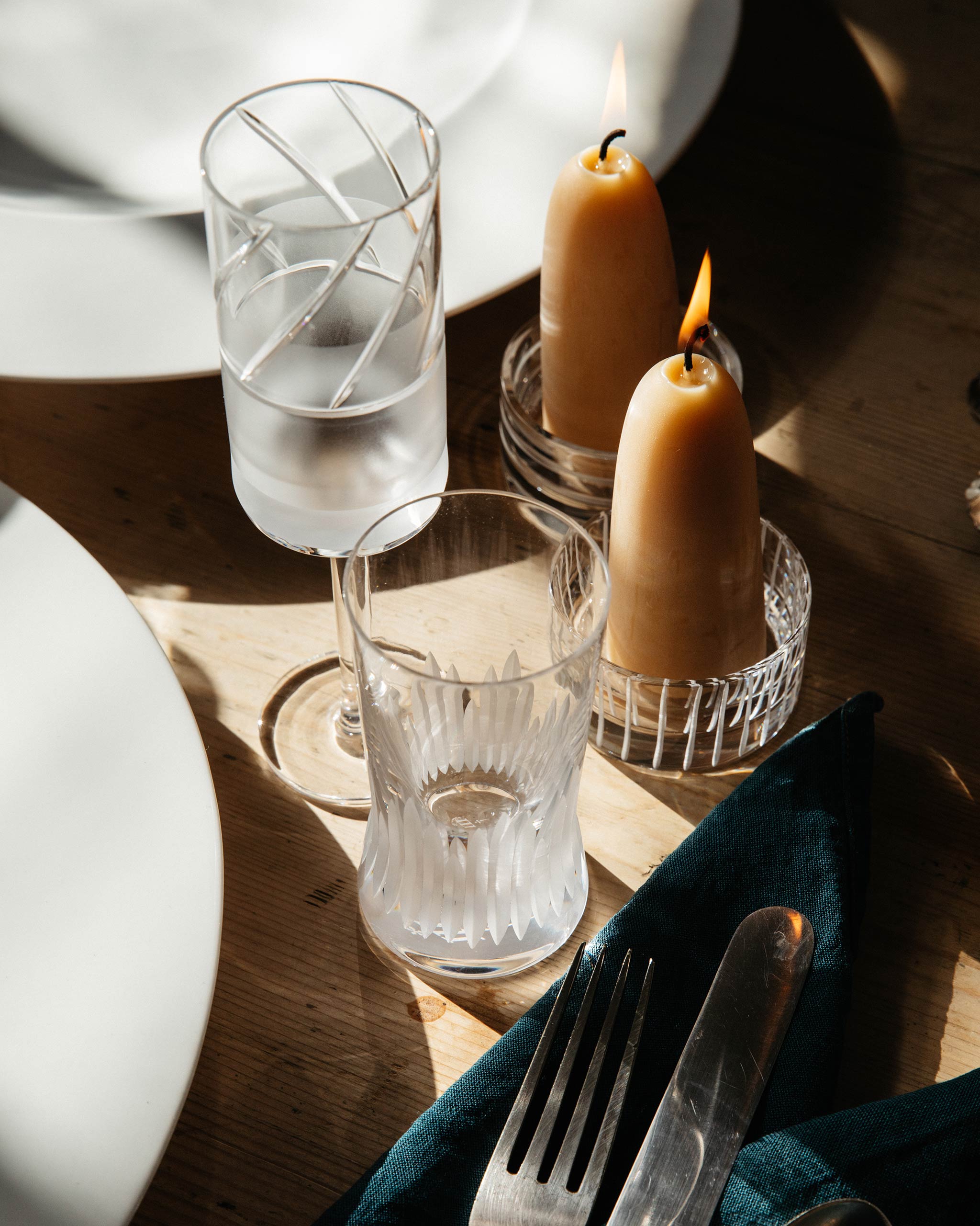Elegant crystal champagne flute on a refined dinner table with plates, cutlery, and burning candles in crystal holders.